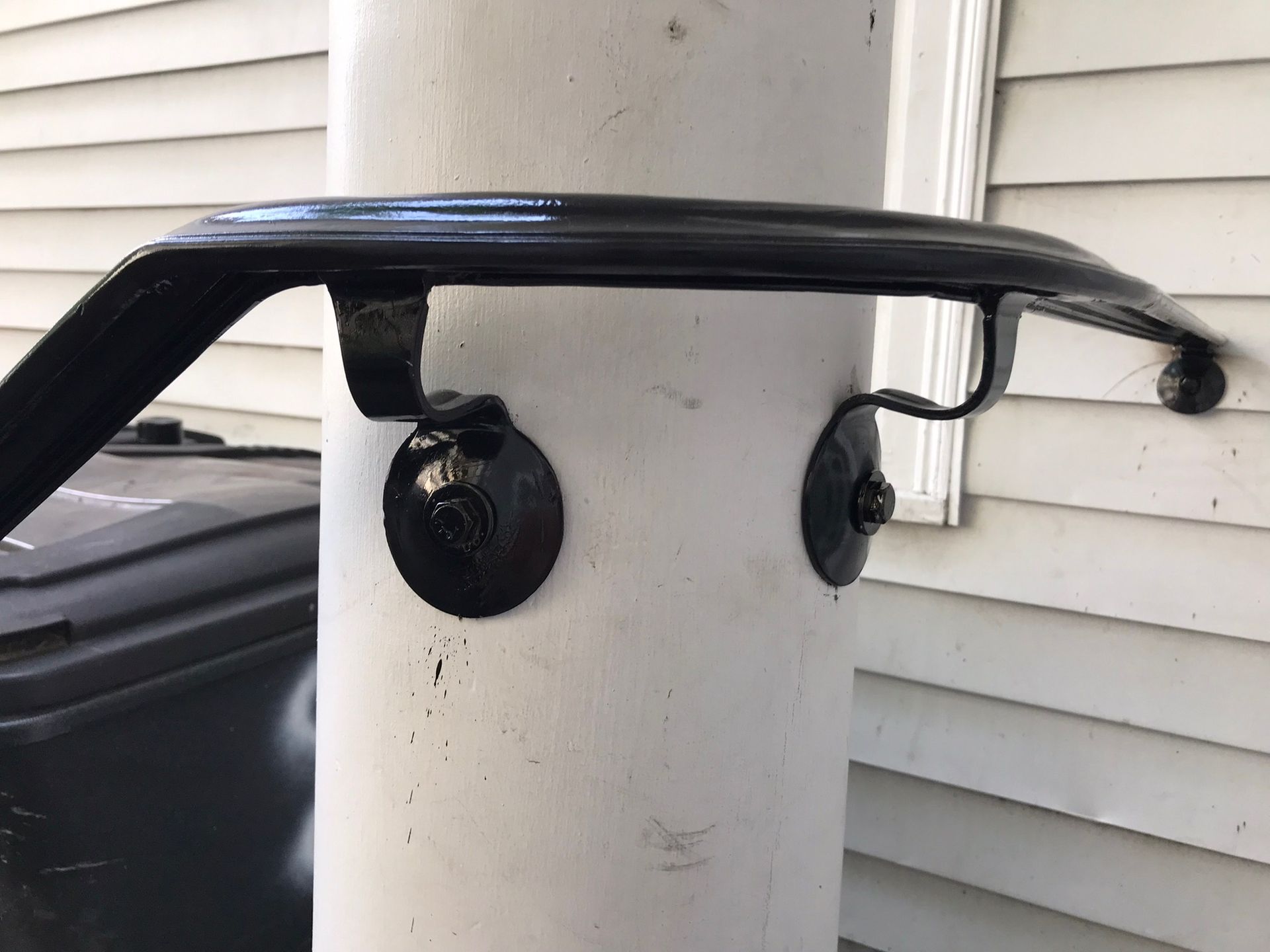 Black metal handrail mounted to a white cylindrical post beside a house wall