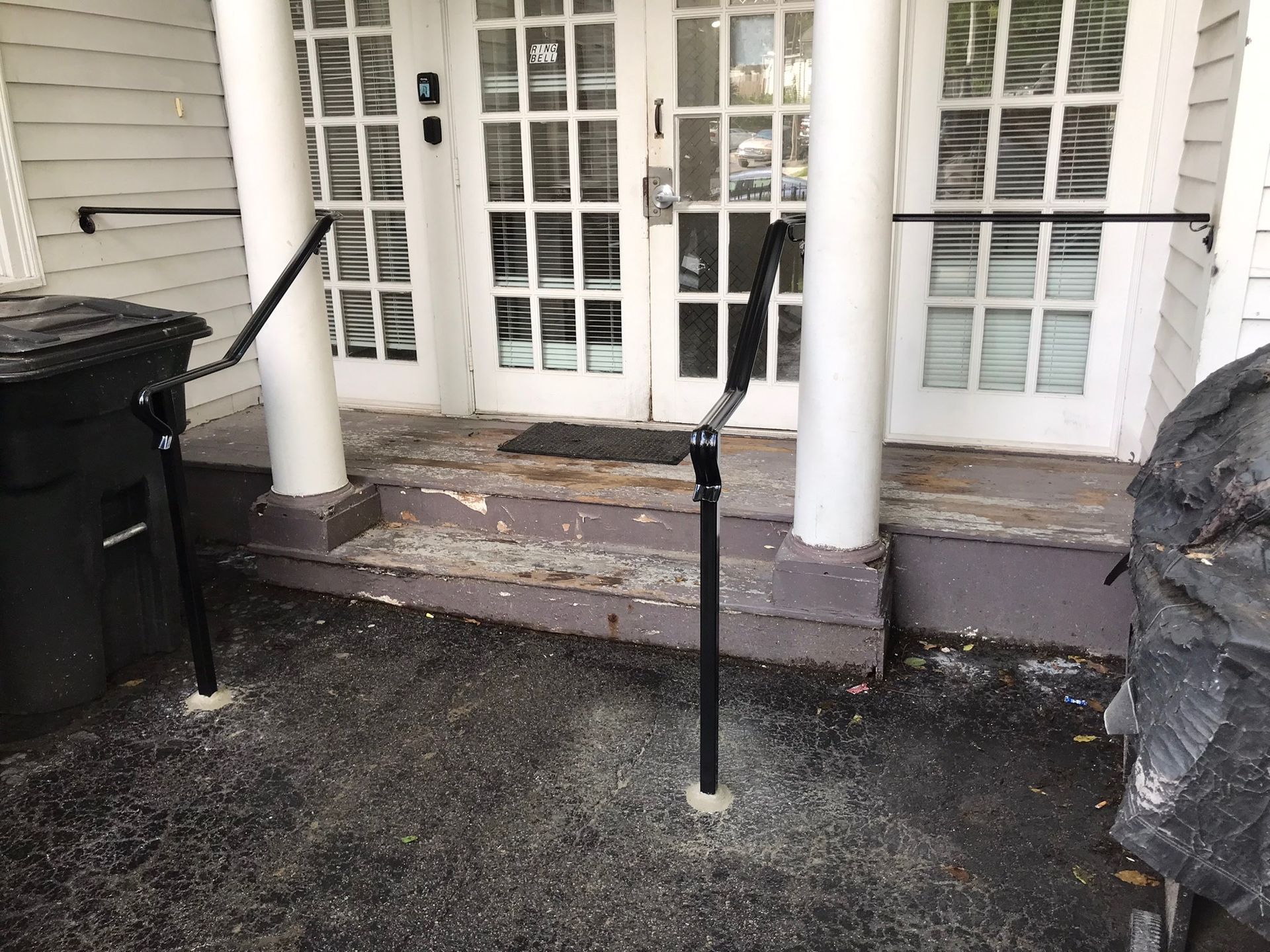Front porch with black accessibility handrails, concrete steps, white columns, and French doors.