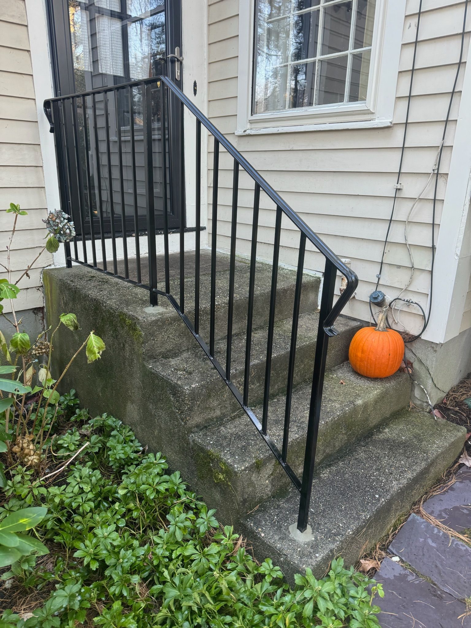 Front steps with black iron railing, weathered concrete, and a small pumpkin by a house entrance.
