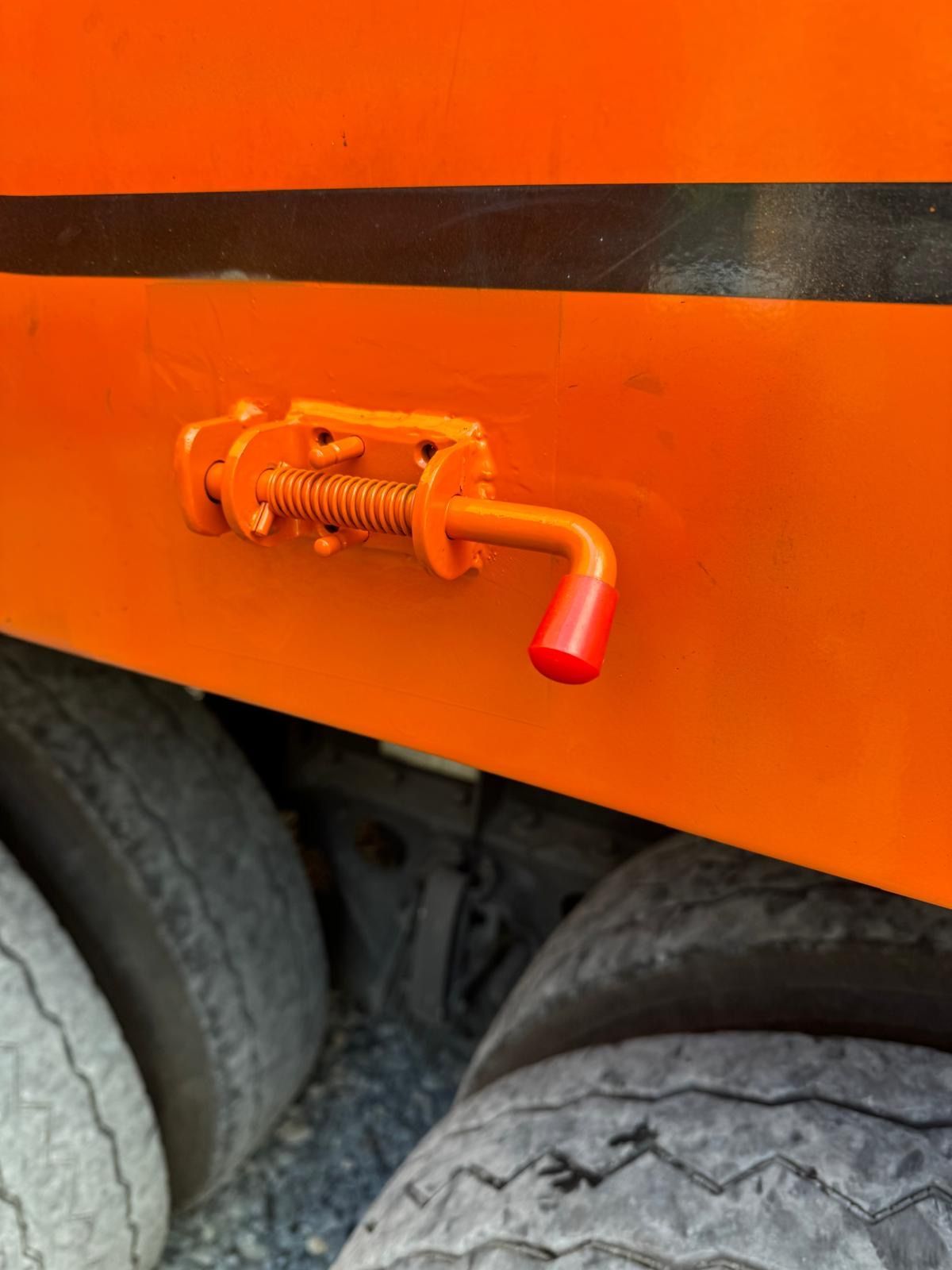 Orange truck side latch with a red handle above a tire.