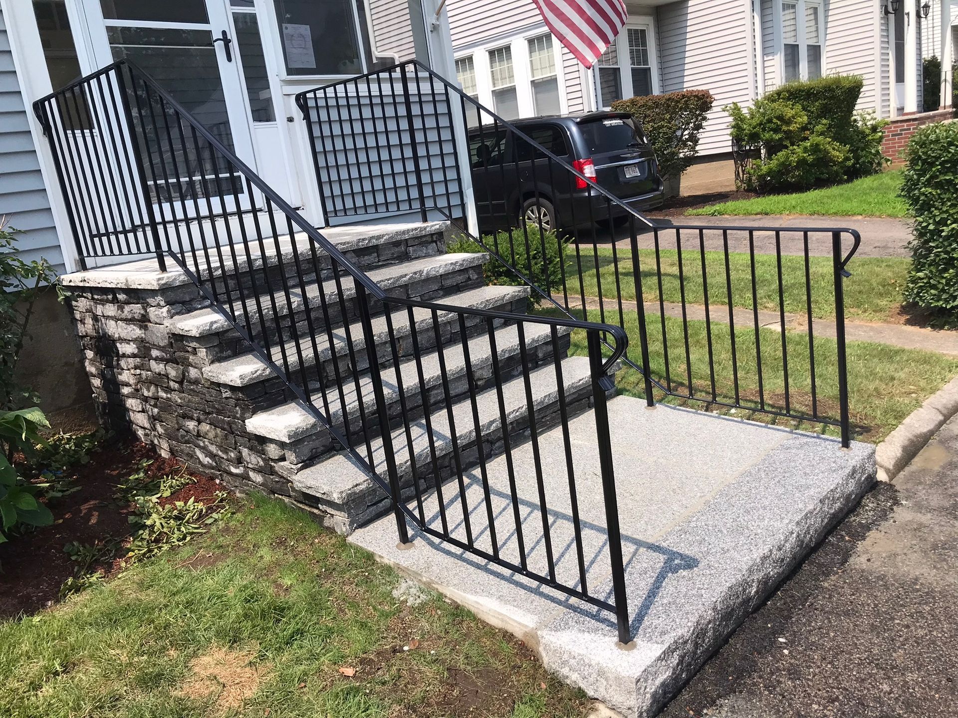 Black metal accessibility ramp with handrails and steps leading to a house entrance.