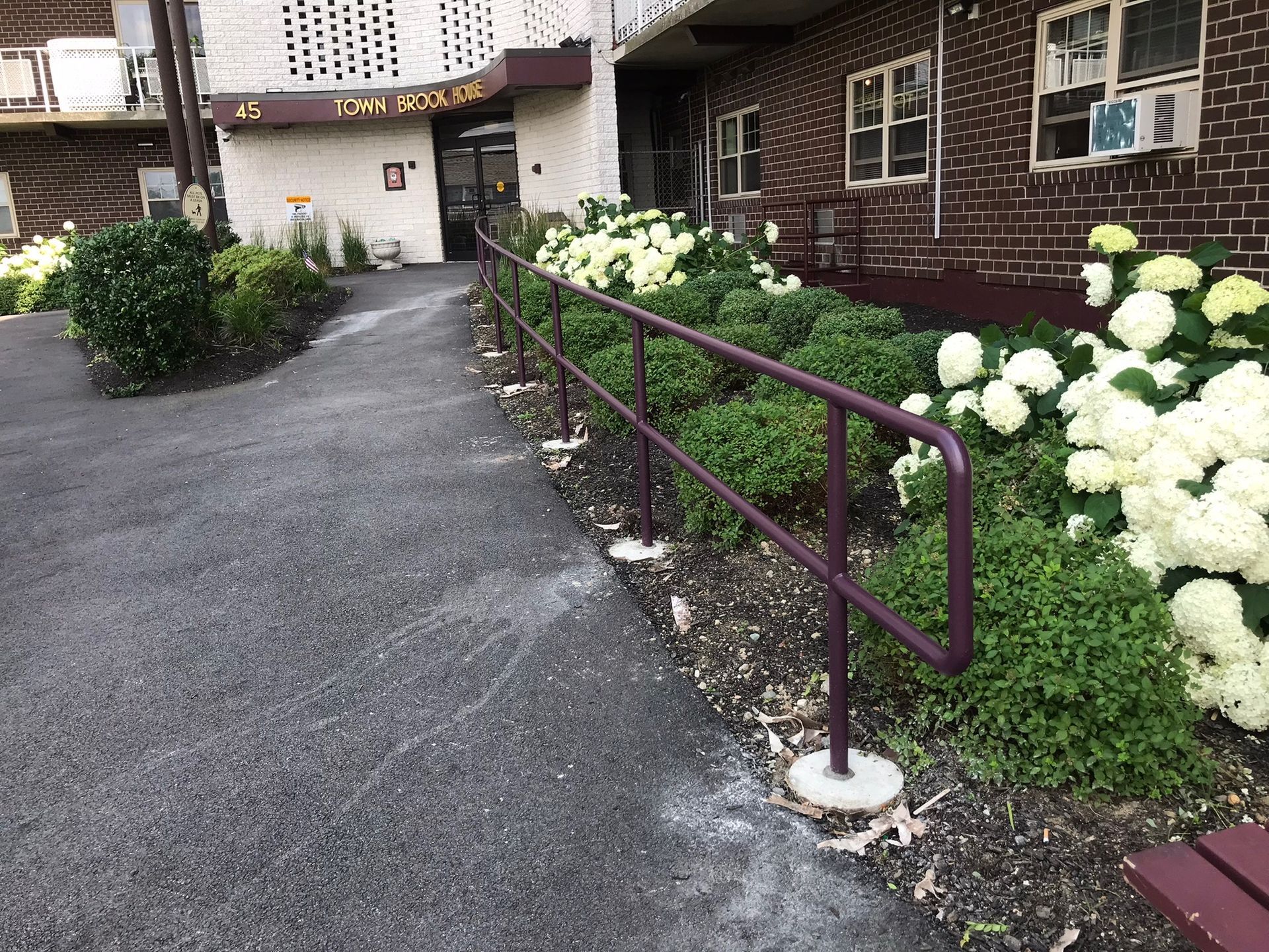 Flower-lined walkway with maroon handrails leading to a brick building entrance
