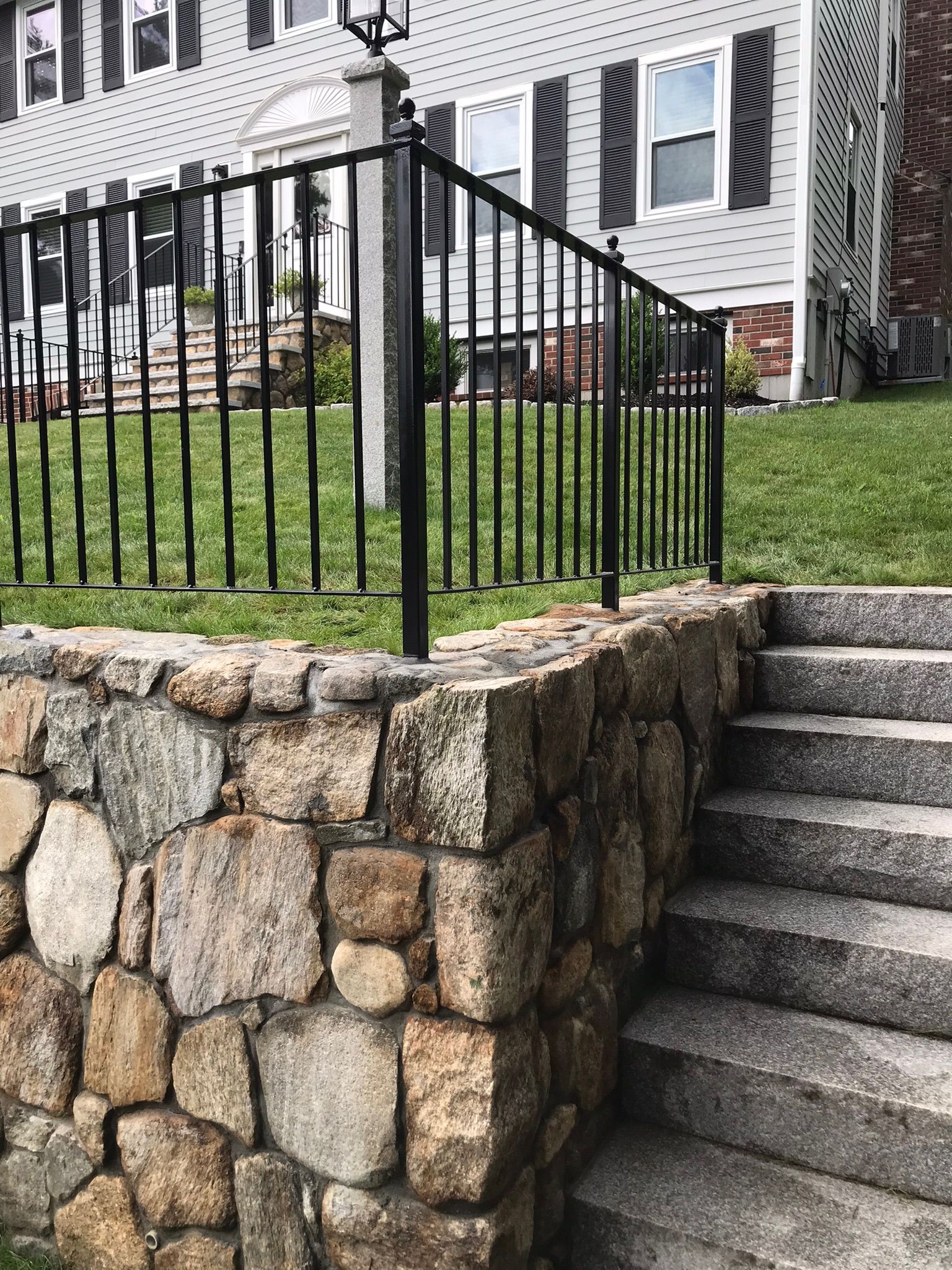 Stone retaining wall beside concrete steps and black metal railing in front of a house.
