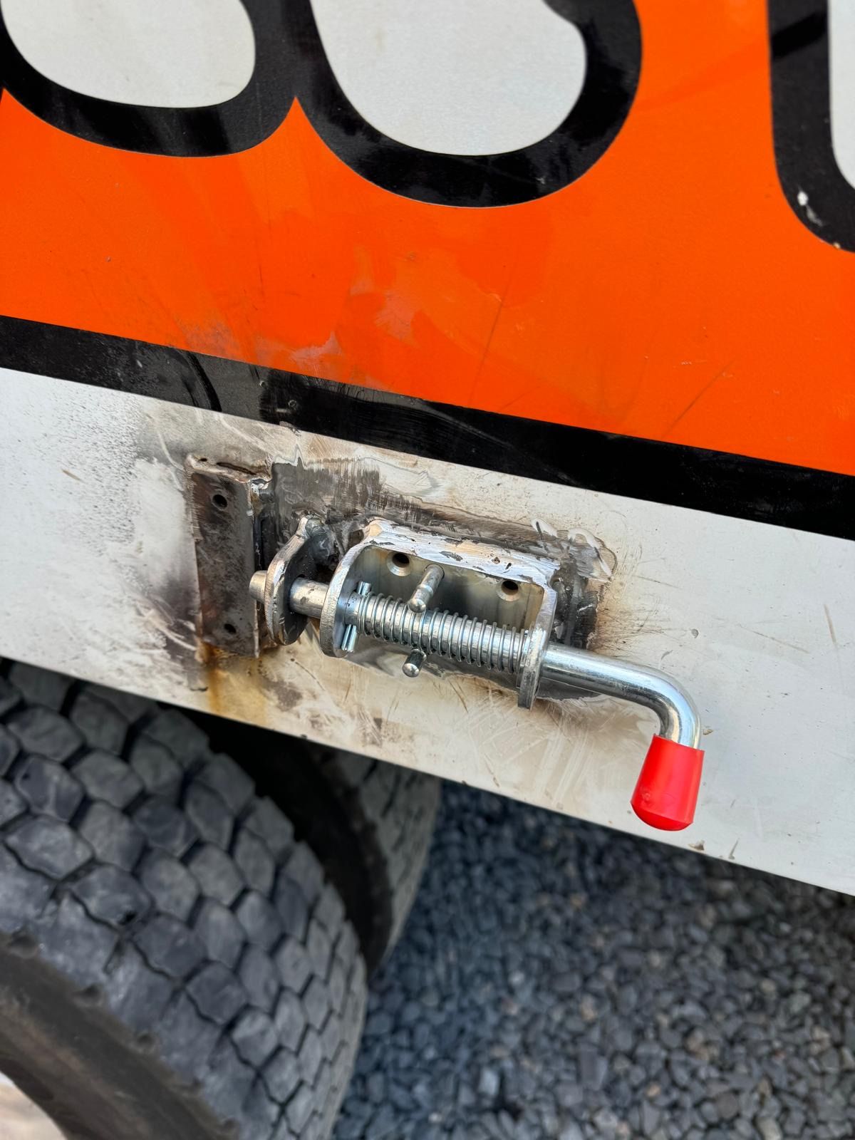 Close-up of a red-handled metal latch on an orange vehicle panel above a tire