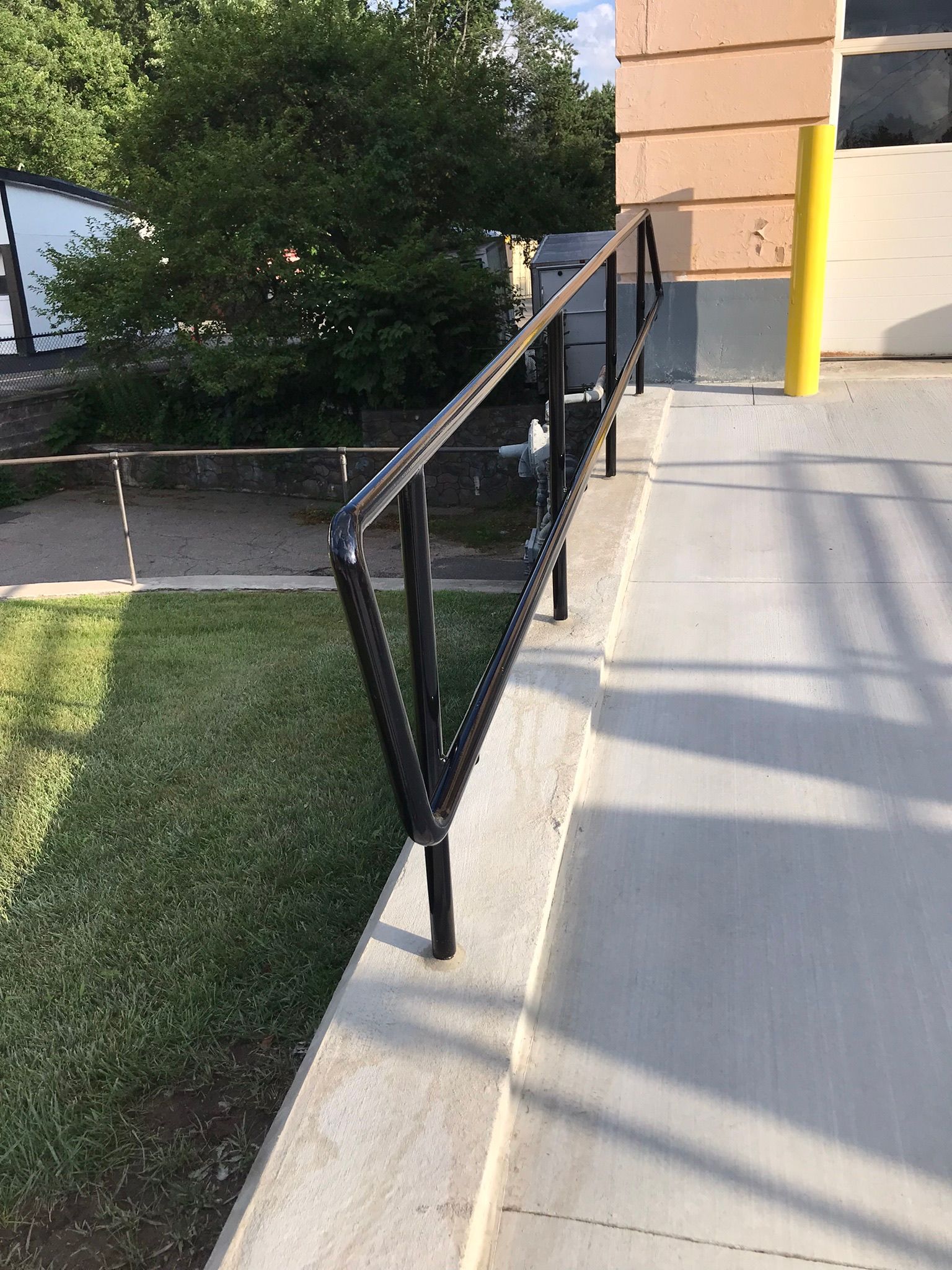 Black metal handrail beside a concrete ramp and sidewalk outside a building