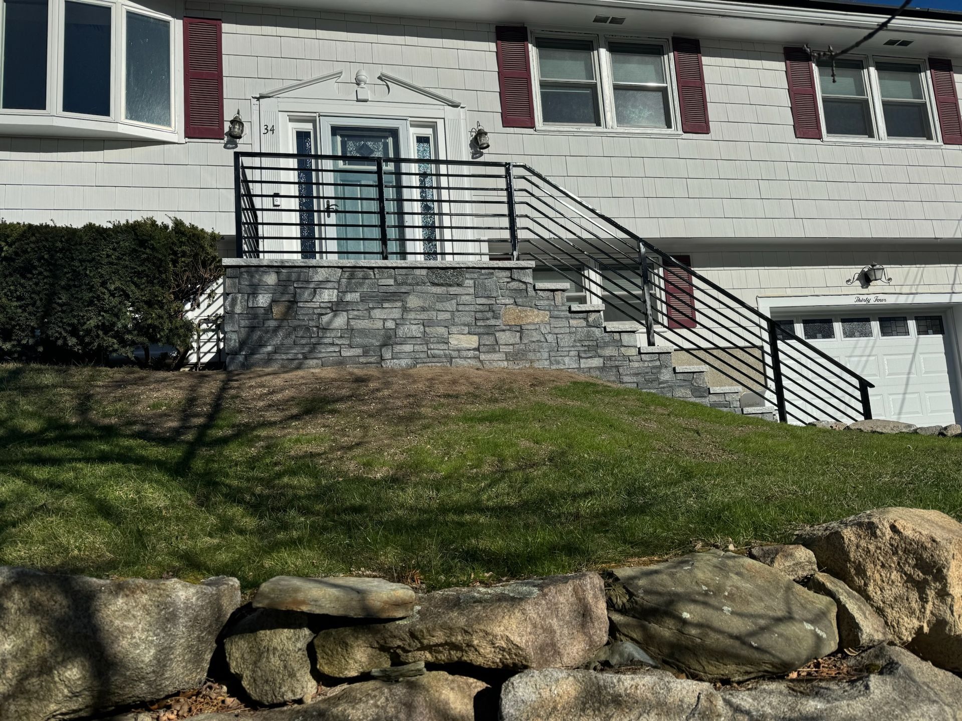 House entrance with stone steps, black railing, and a grassy slope in front