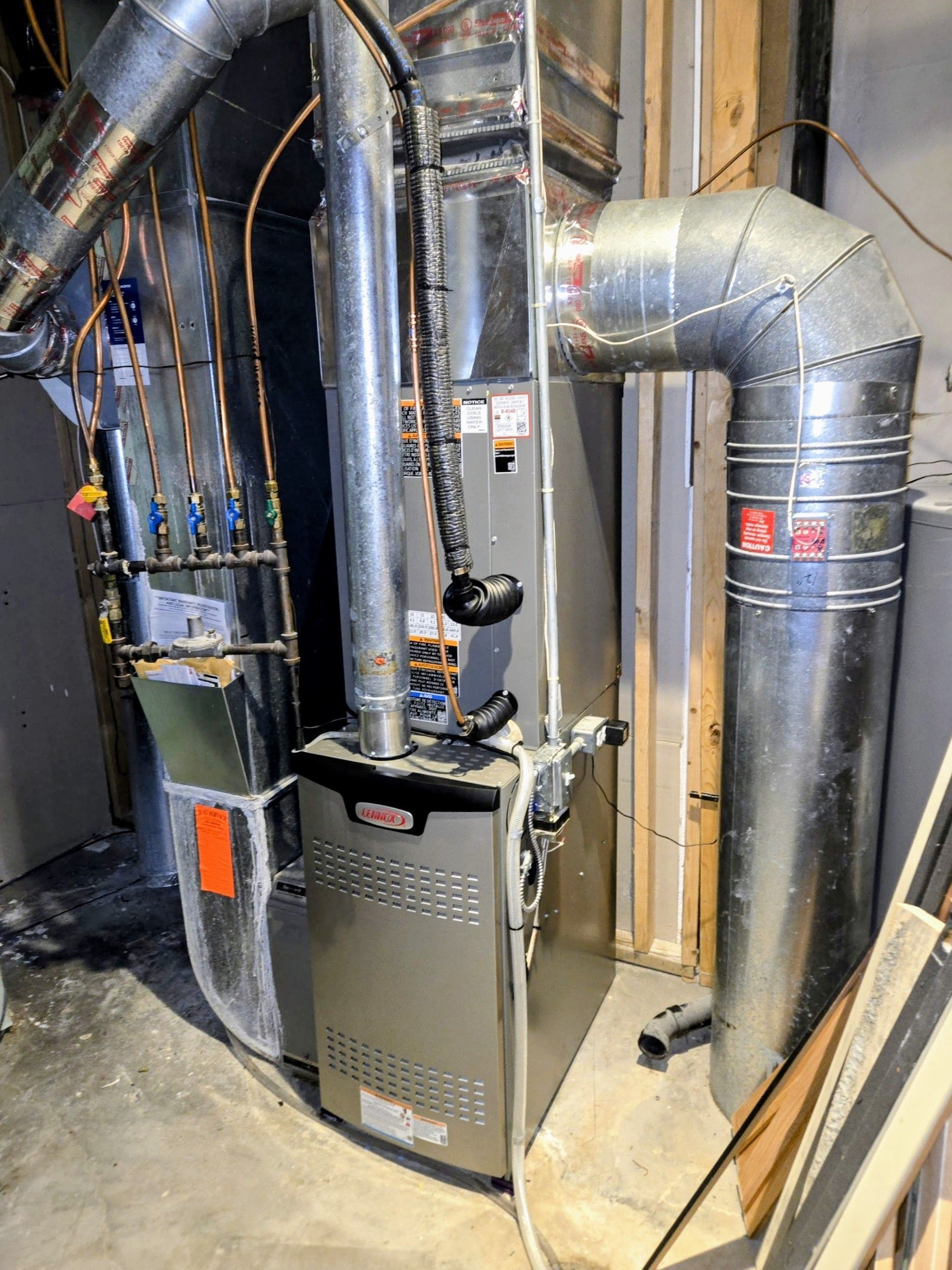 Furnace and ductwork in a basement utility room with exposed pipes and metal vents