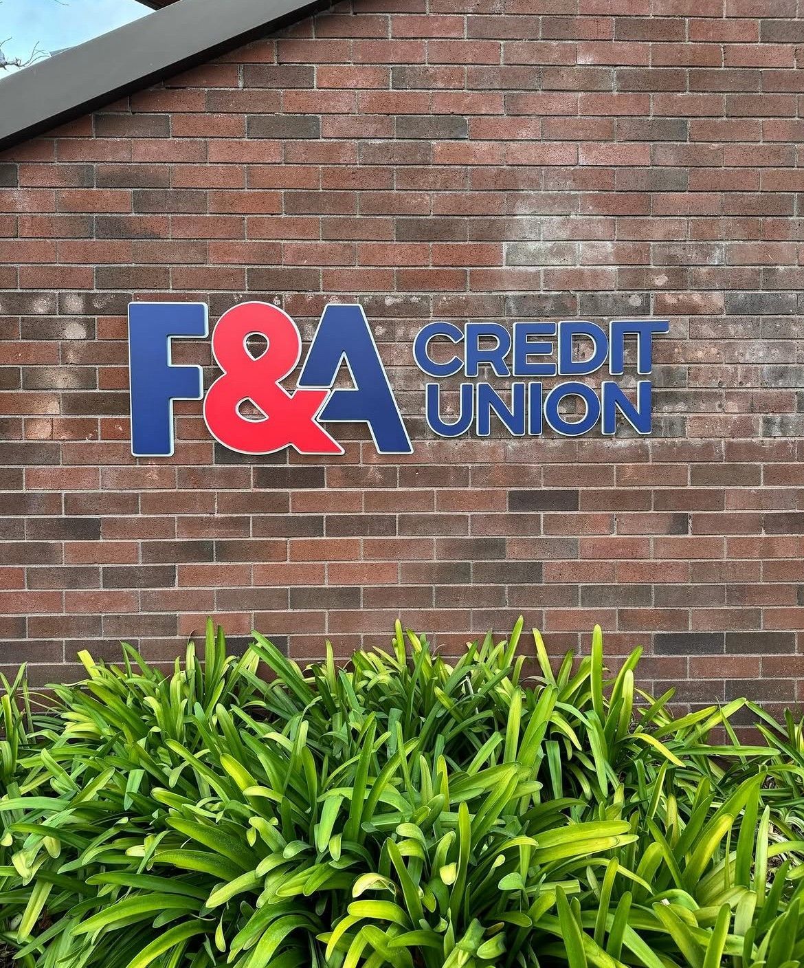 F&A Credit Union sign on a brick wall above green shrubs