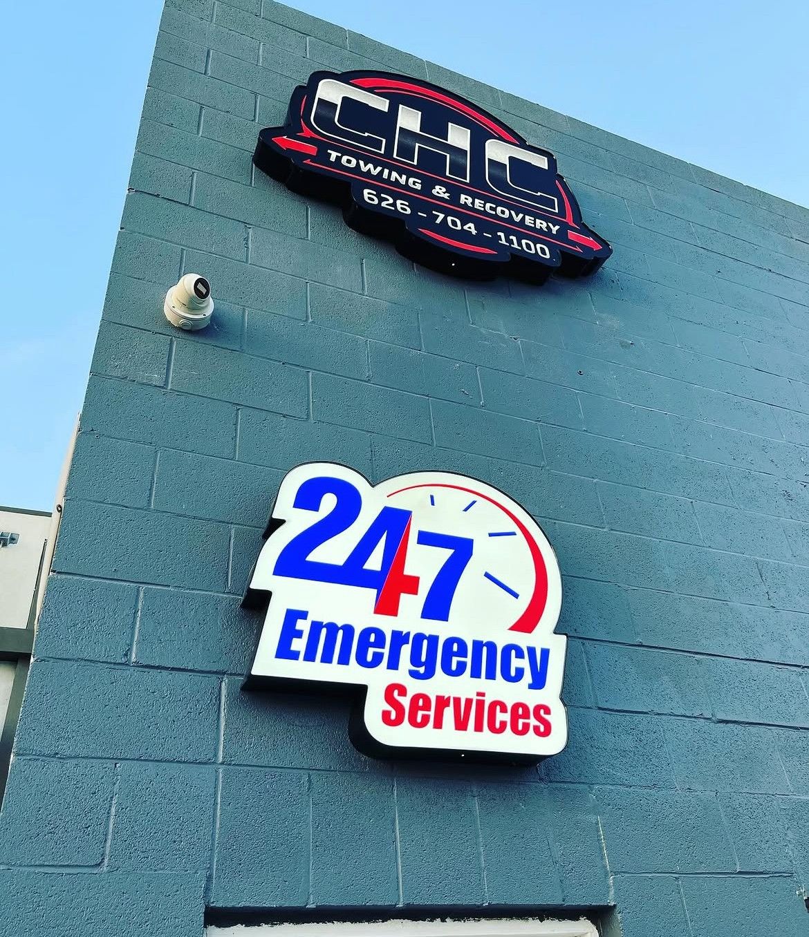 Blue building wall with 247 Emergency Services sign and a black-red logo above it