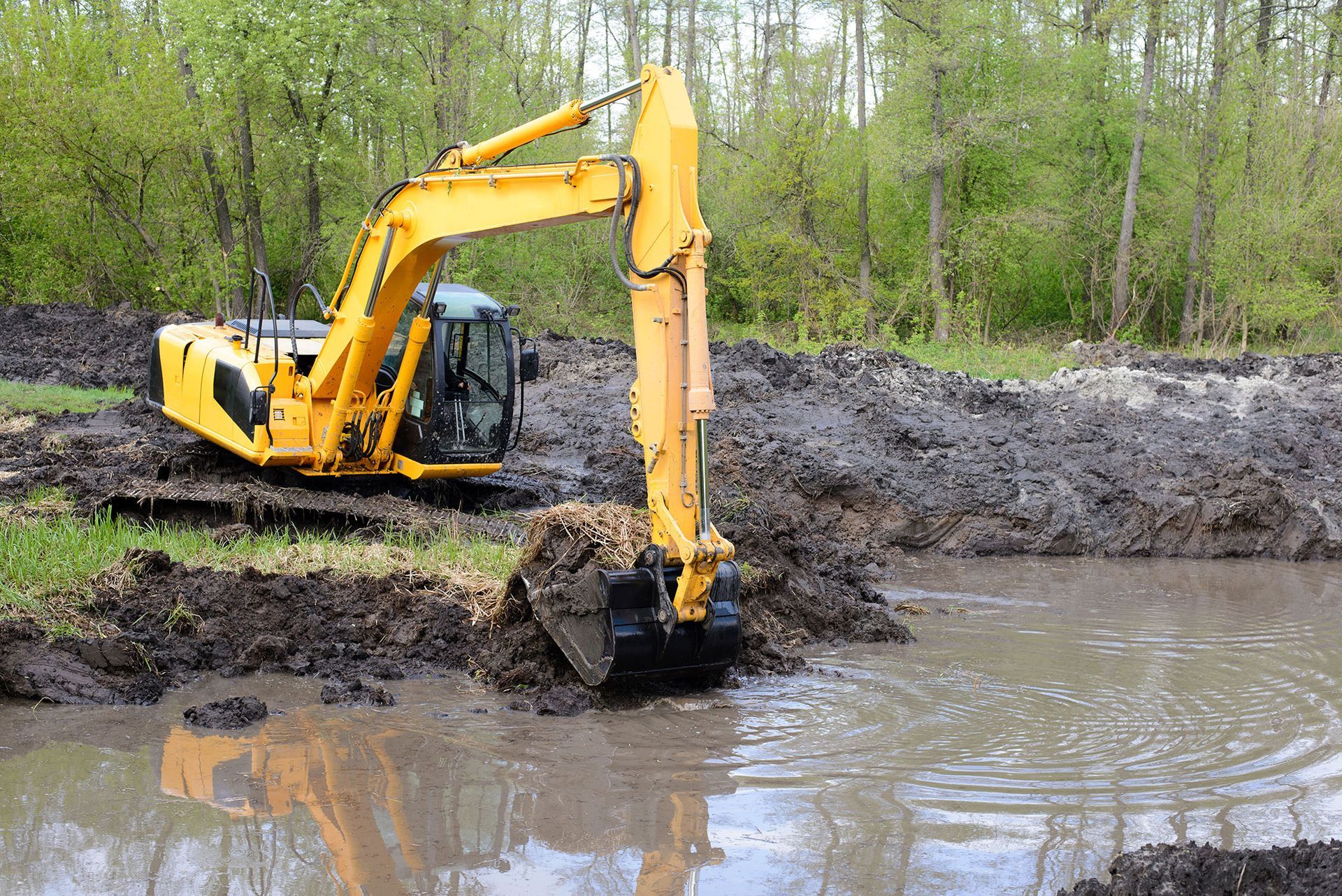 A yellow excavator is digging a muddy pond.