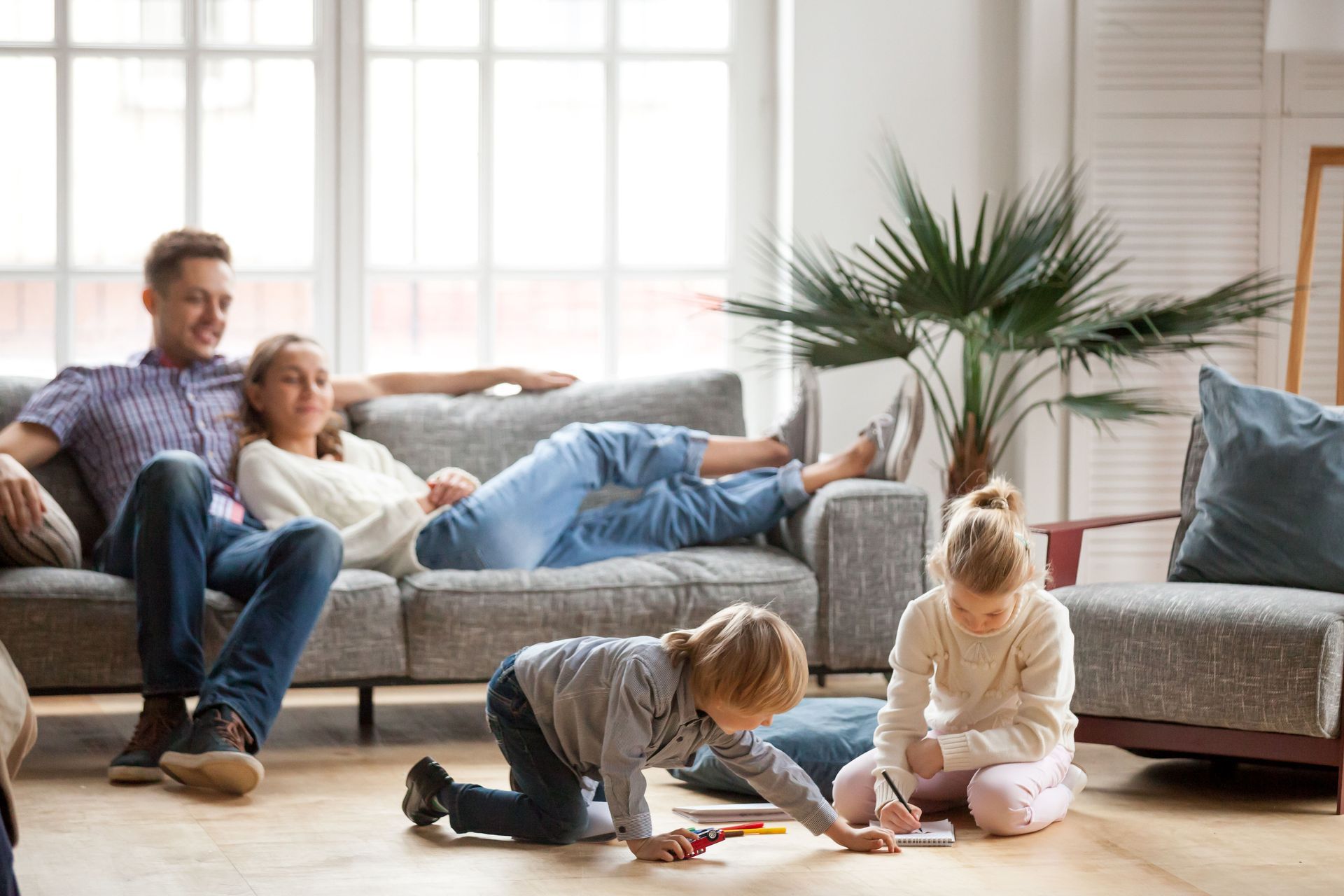 Family relaxing in living room: parents on couch, children playing on floor.
