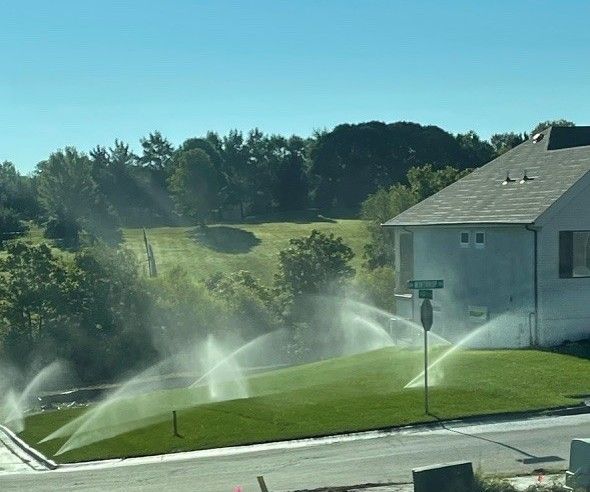 Sprinklers watering a green lawn in front of a house on a sunny day.