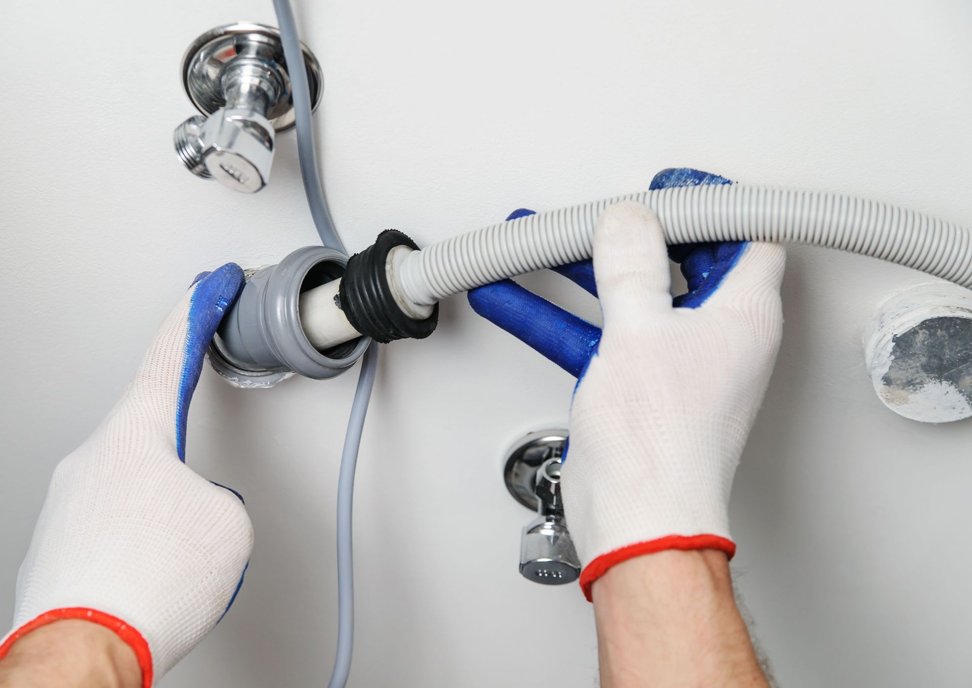 Gloved hands connect a gray flexible hose to a chrome plumbing fixture under a sink.