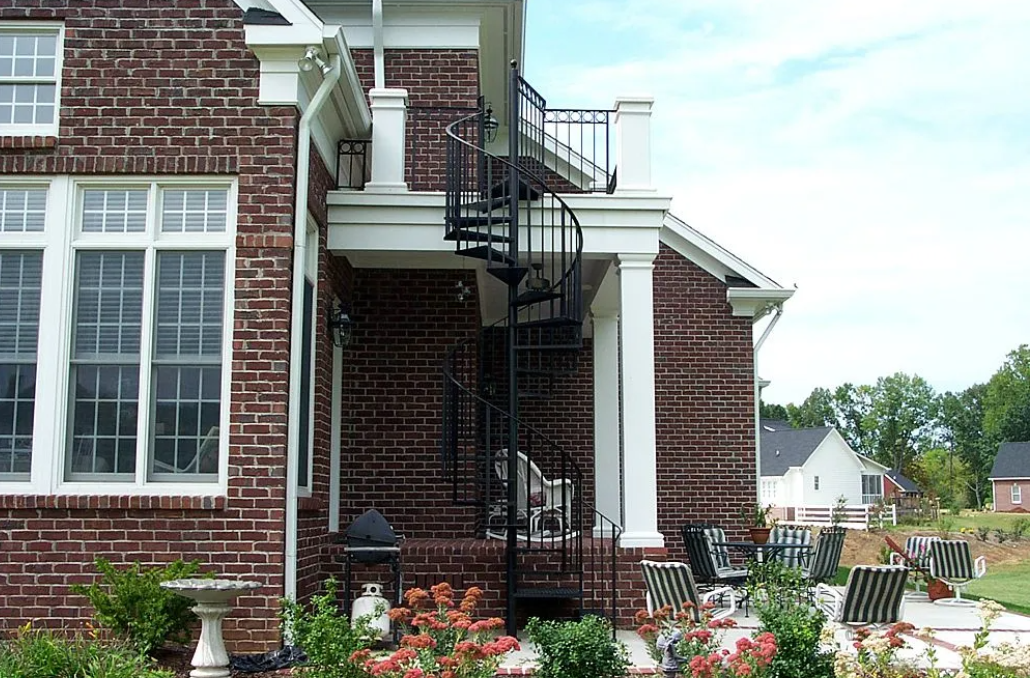 Black spiral staircase with ornate railing against a white wall.