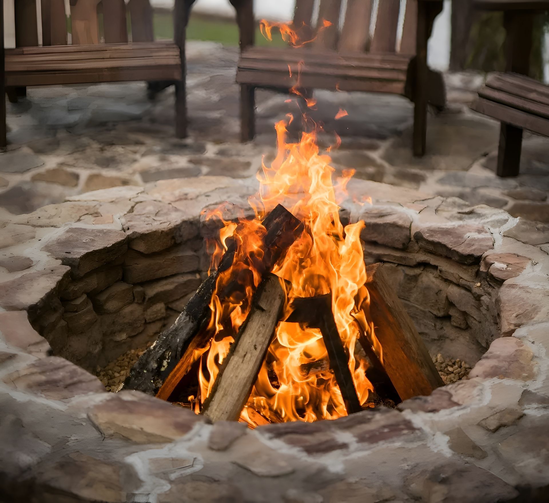 Fire pit with burning logs, surrounded by stone and wooden chairs.