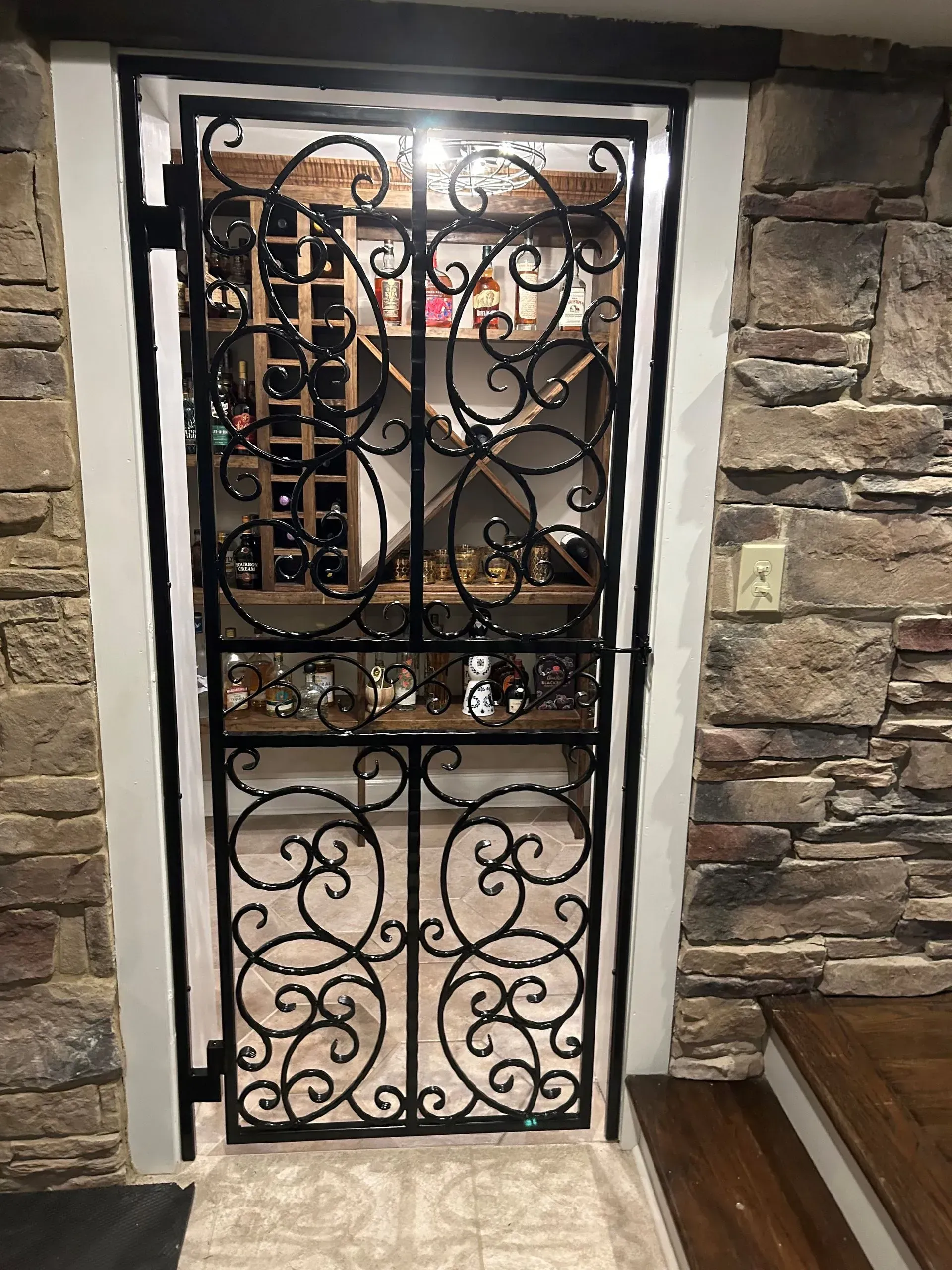 Black wrought iron gate leading into a wine cellar, set in a stone wall.