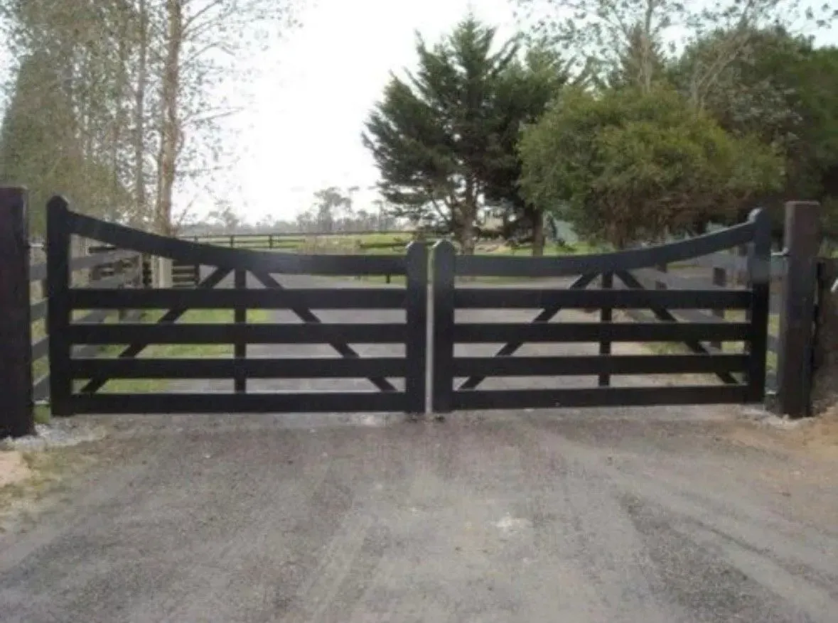 Black wooden double gates on a gravel driveway, with trees in the background.