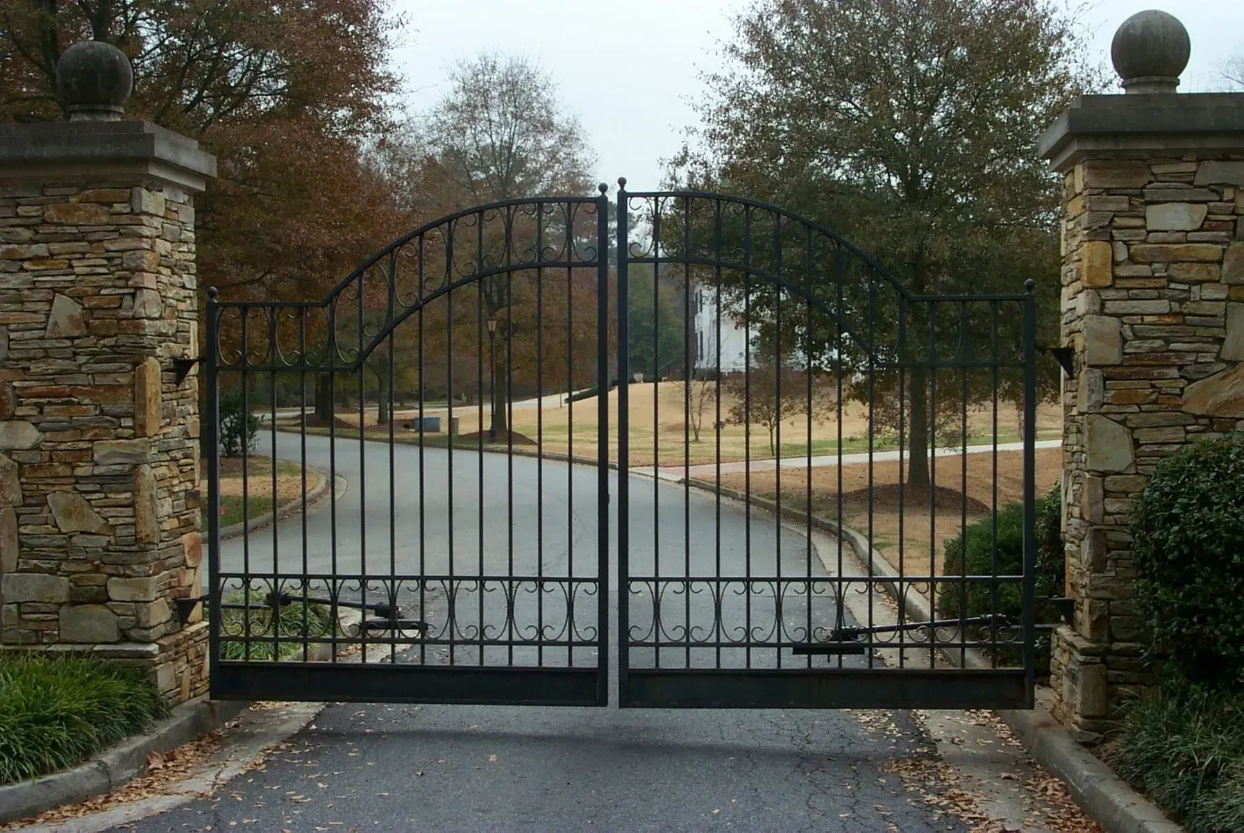 Black wrought iron gate set between stone pillars, leading to a tree-lined driveway.