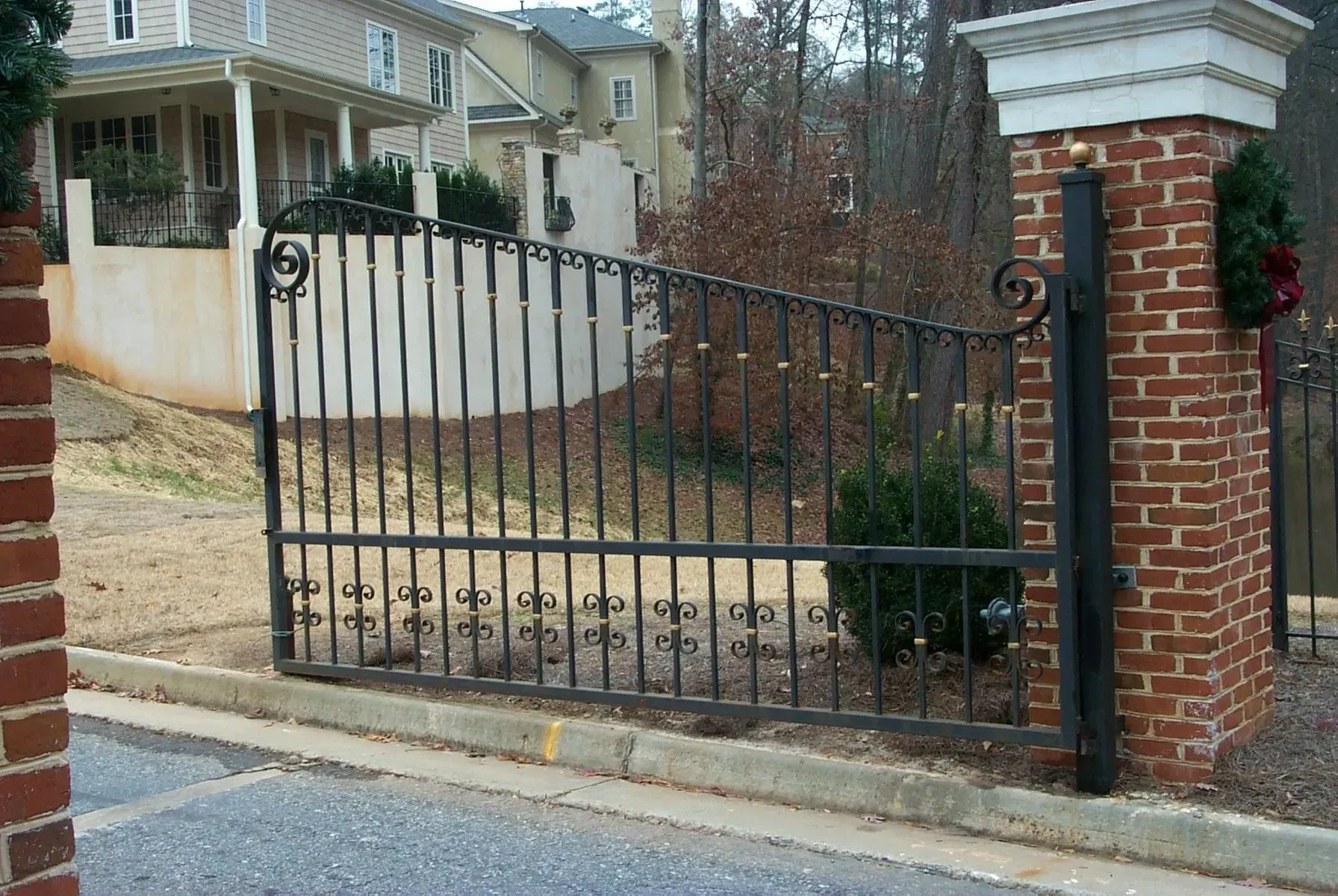 Black iron gate set in brick columns, leading to a residential area.