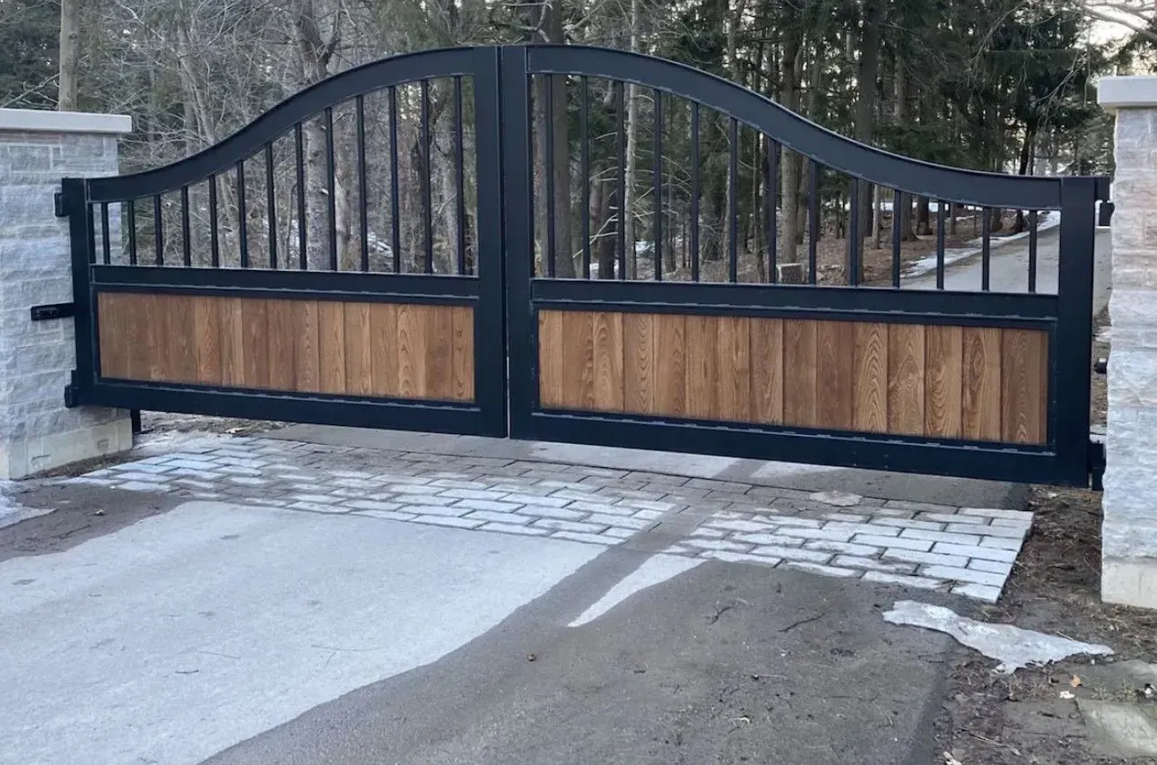 Black wrought iron gate with wooden panels, arched top, set between stone pillars.