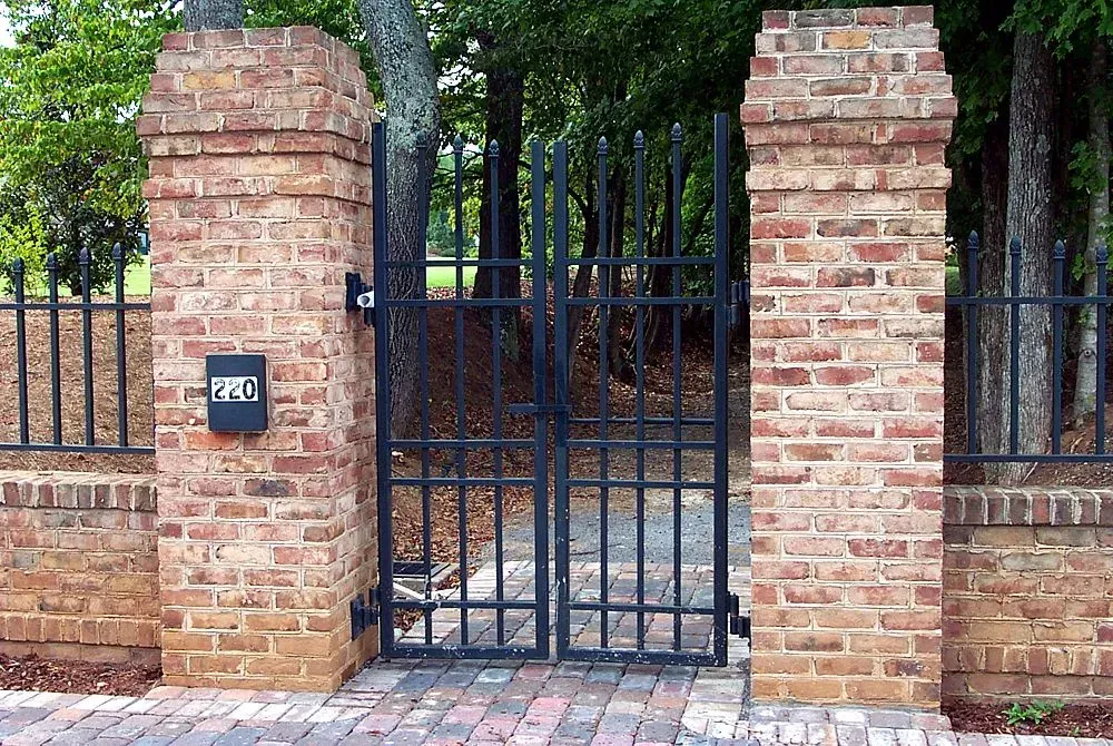 Brick pillars with a black metal gate and fence.