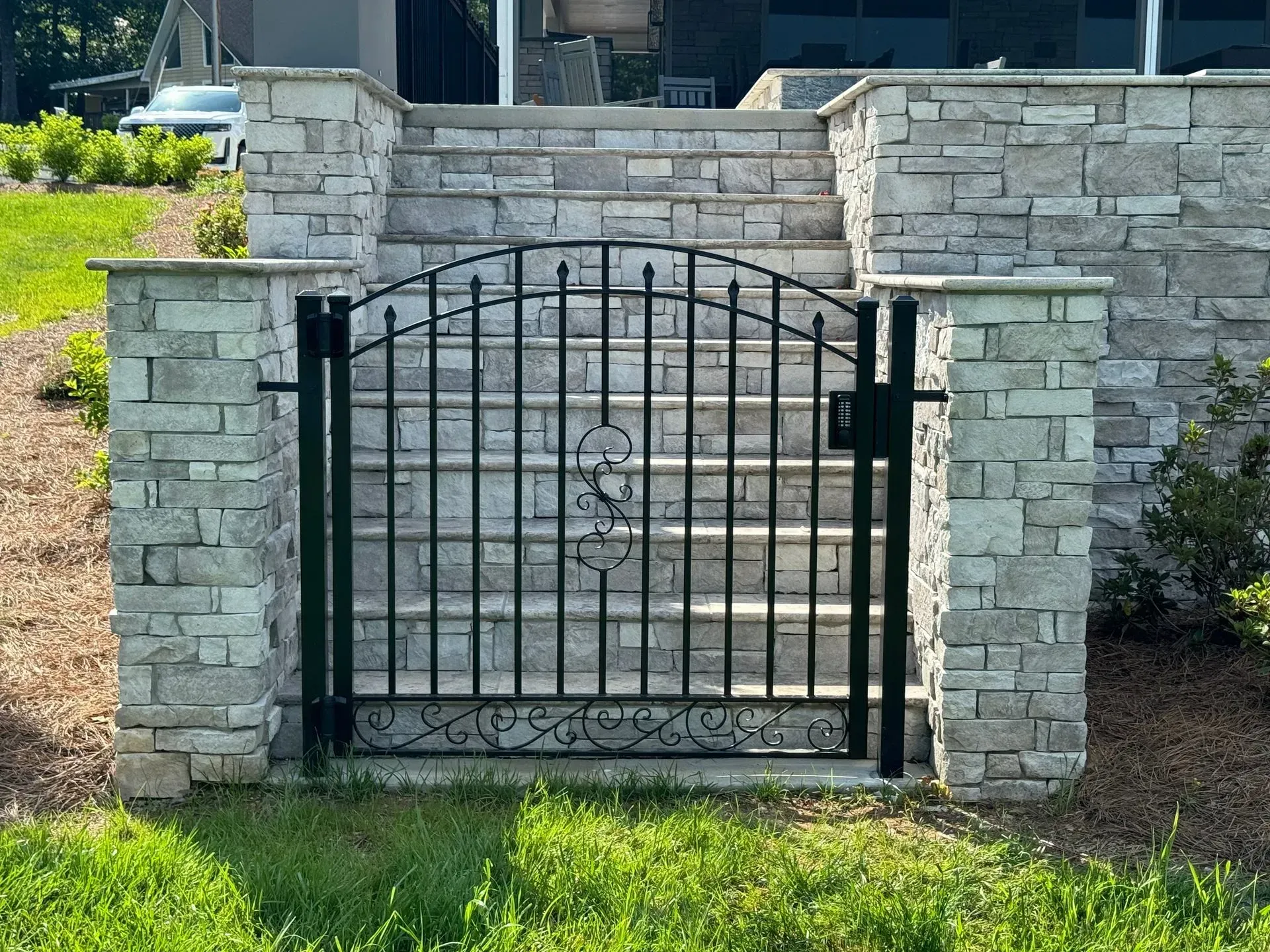 Black metal gate with decorative scrollwork between stone pillars leading to steps.