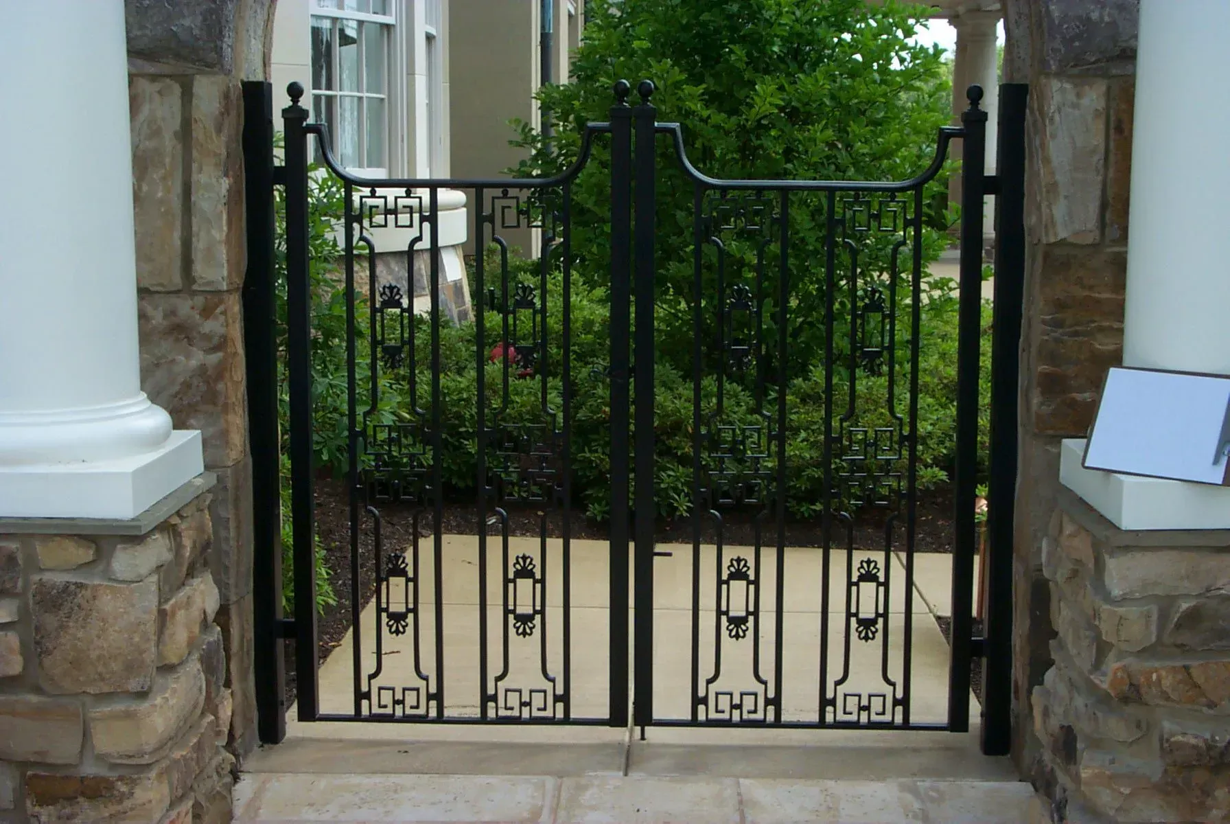 Black wrought iron double gate set between stone columns, leading to a garden.