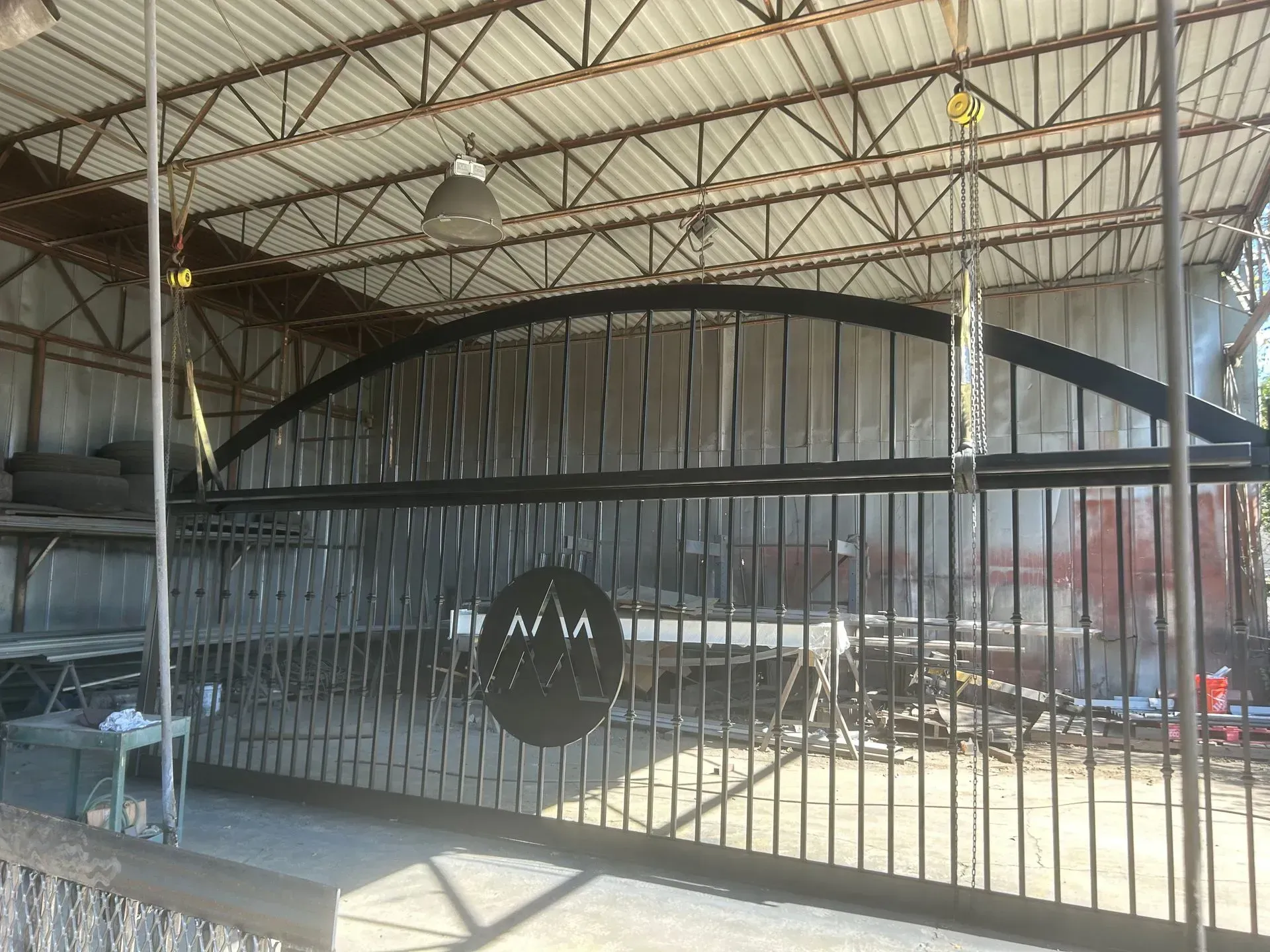 Black metal arch gate with vertical bars and a circular emblem, under a corrugated roof.