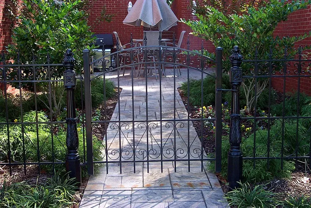 Black wrought iron gate leading to a backyard patio with a table, chairs, and an umbrella.