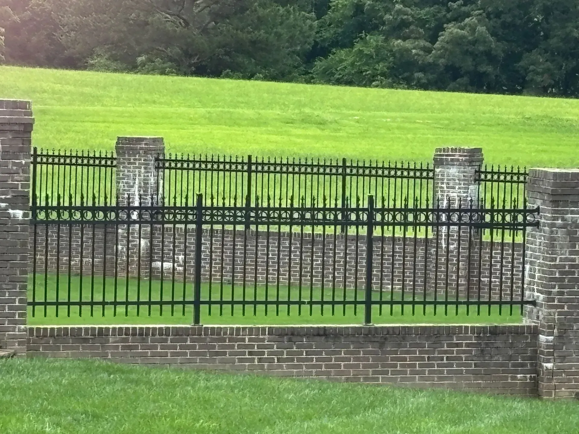Black metal fence with brick pillars and a green grassy background.