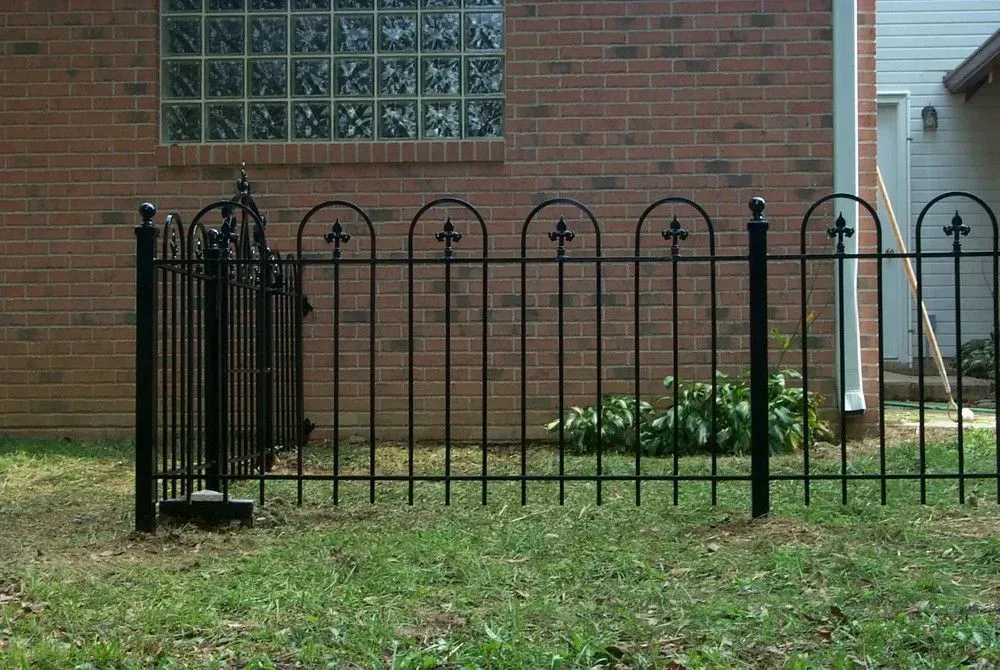 Black wrought-iron fence in front of a brick building with a glass block window; green grass in foreground.