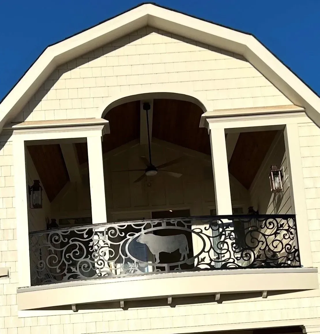 Balcony with ornate metal railing and arched opening; tan building with blue sky.