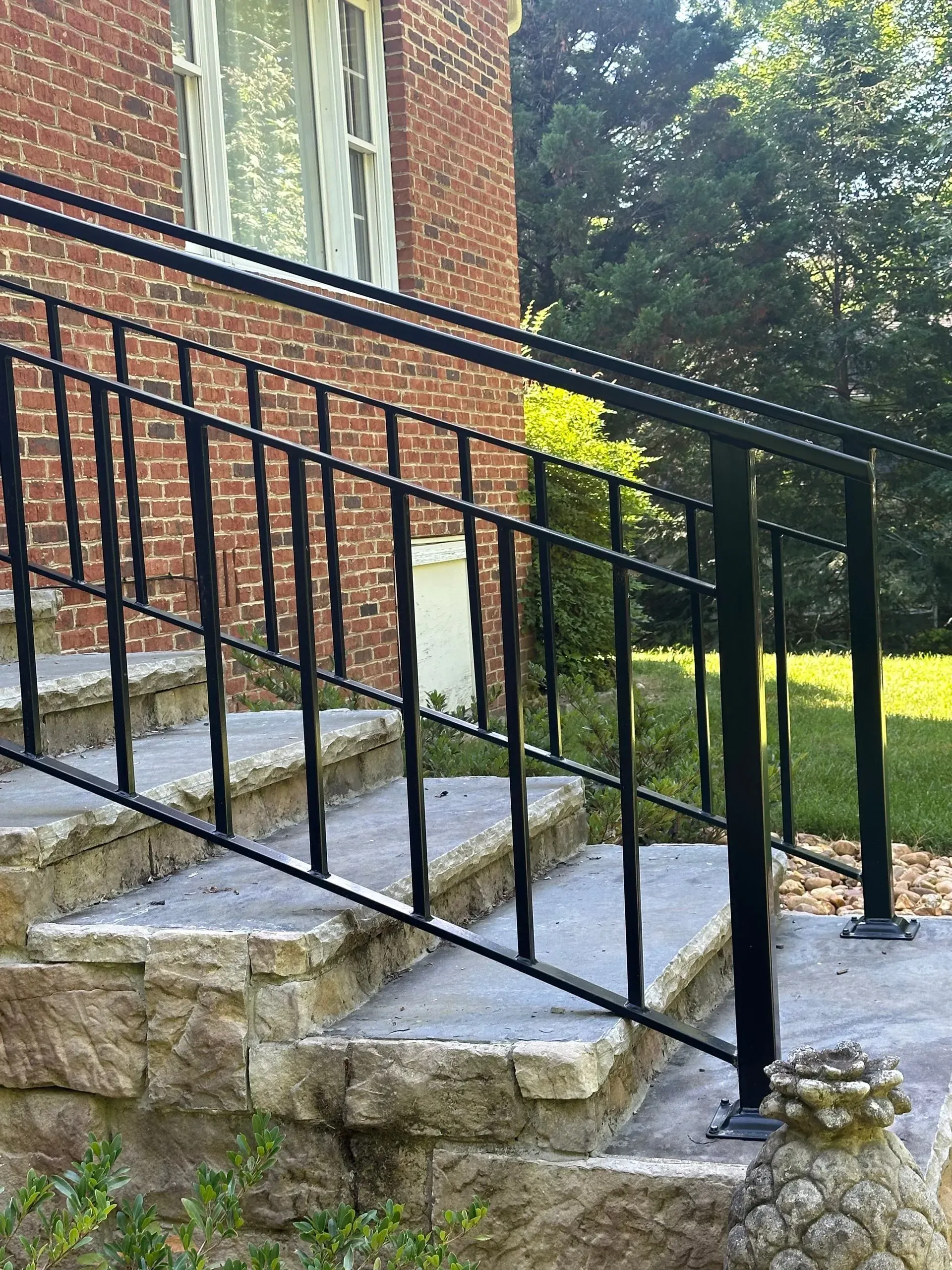 Black metal handrails on stone steps leading up to a red brick building with a window.