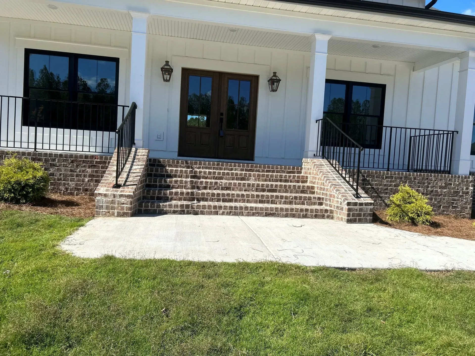 White building with porch, brick steps, black railings, and glass doors. Grass in foreground.