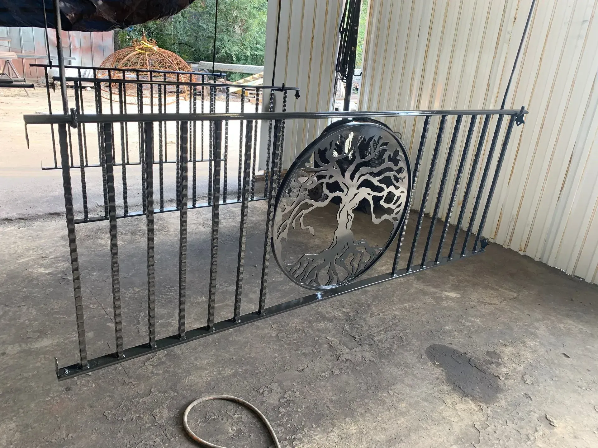 Black metal railing with a tree-of-life design and vertical bars. Outdoors, on concrete.