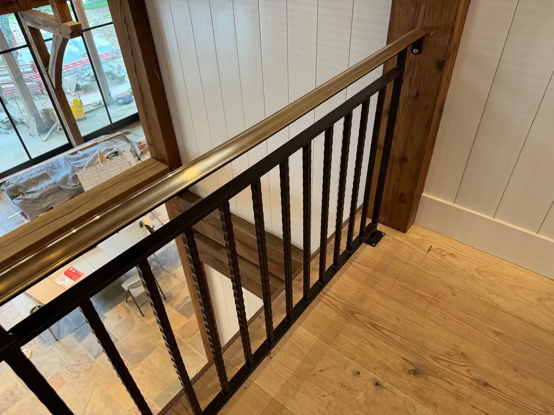 Black metal railing with gold top rail on a second story landing, wood floors and white paneled walls.