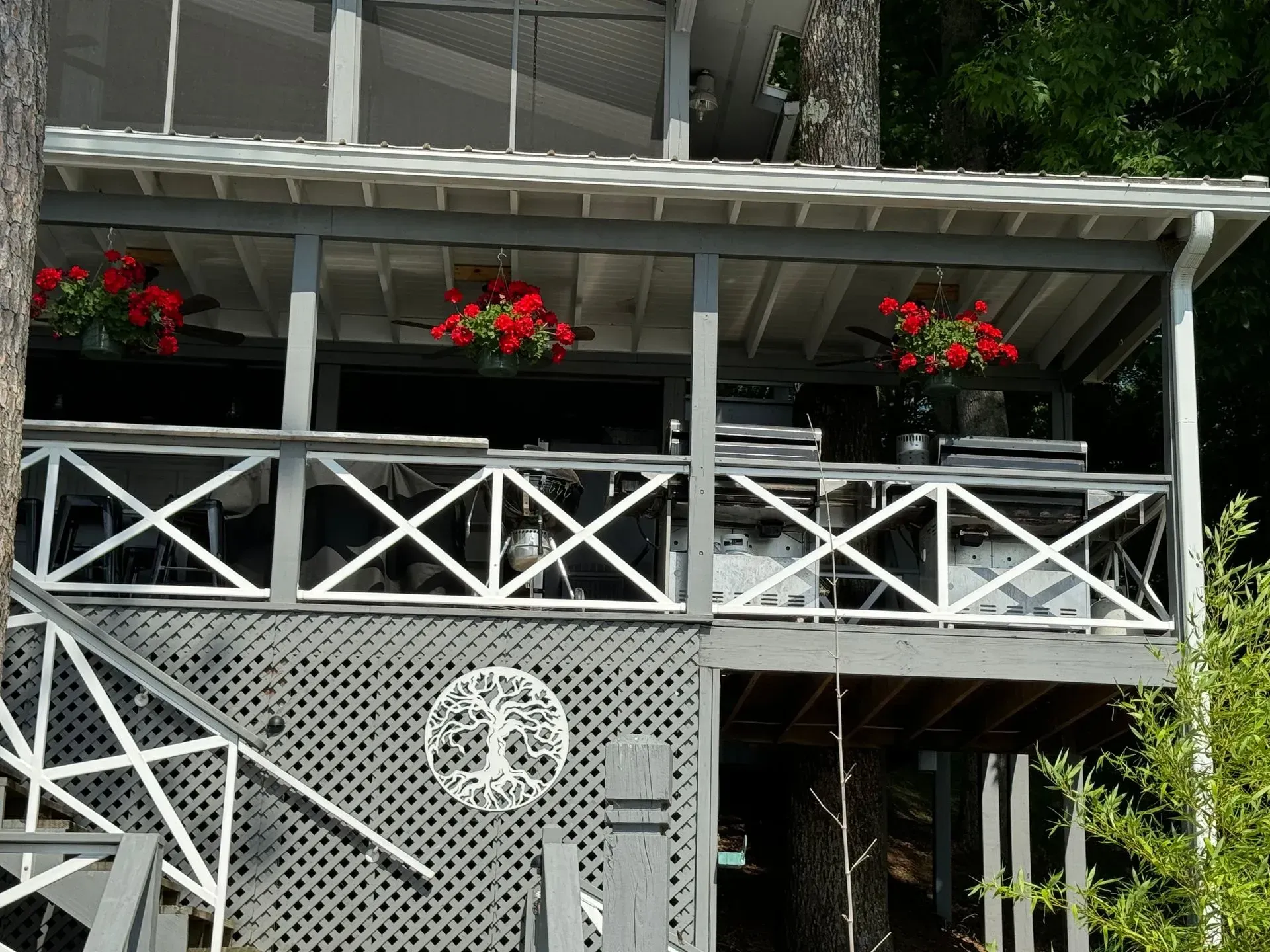 Gray and white elevated porch with red flower baskets, overlooking a body of water.