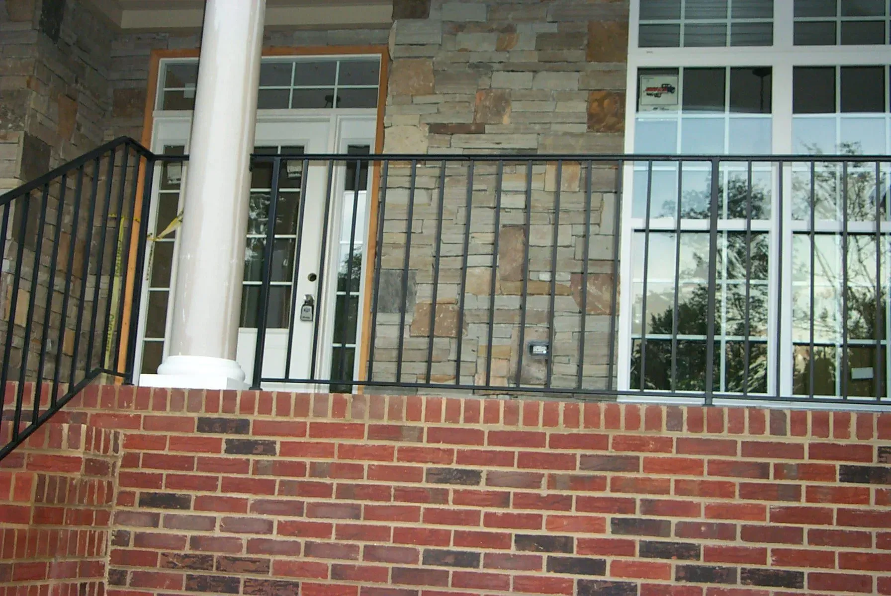 Black metal railing on red brick and stone facade of a building with white doors and windows.