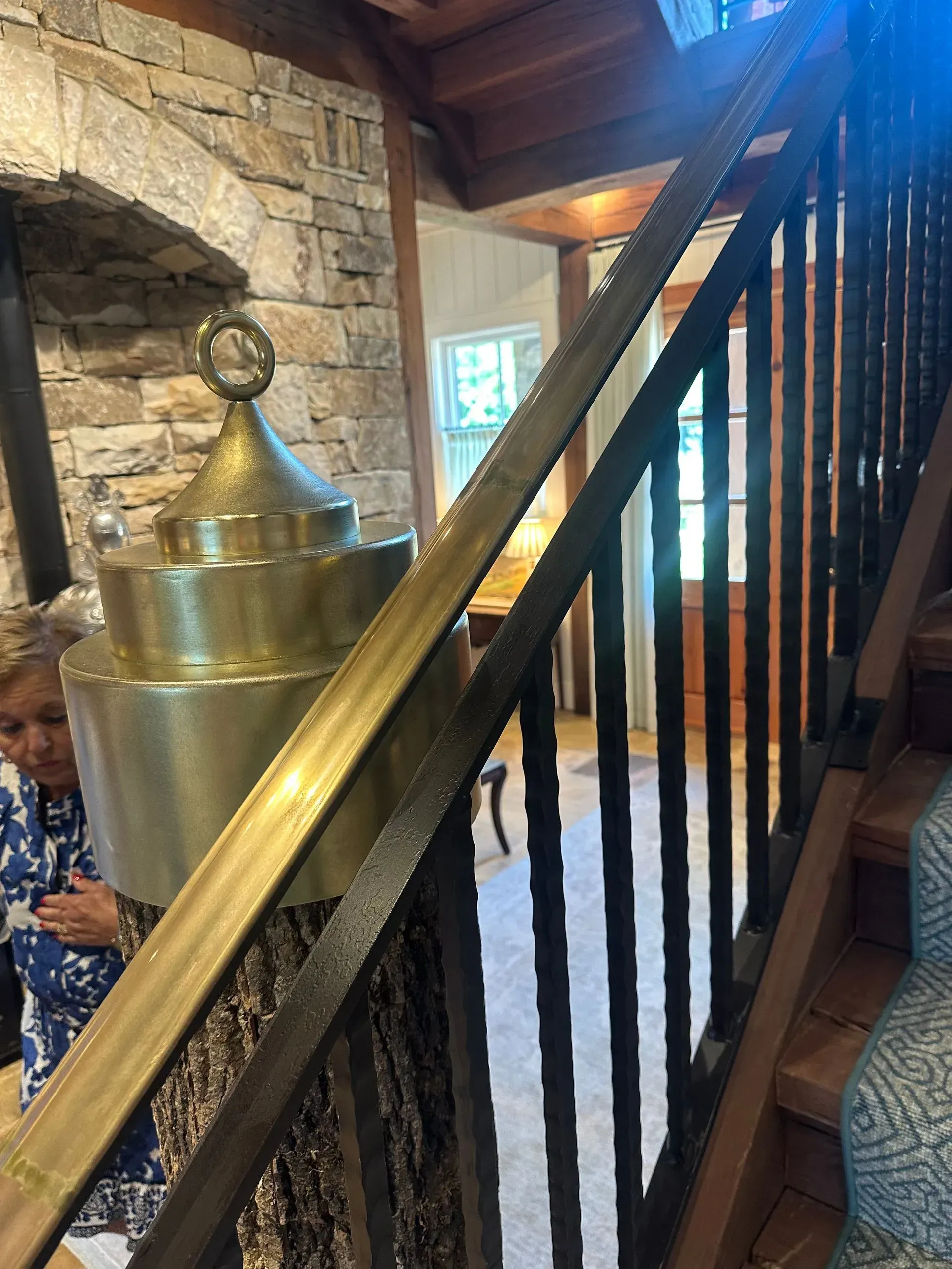 Staircase with dark spindles and brass railing, next to a large brass sculpture. A woman stands nearby.