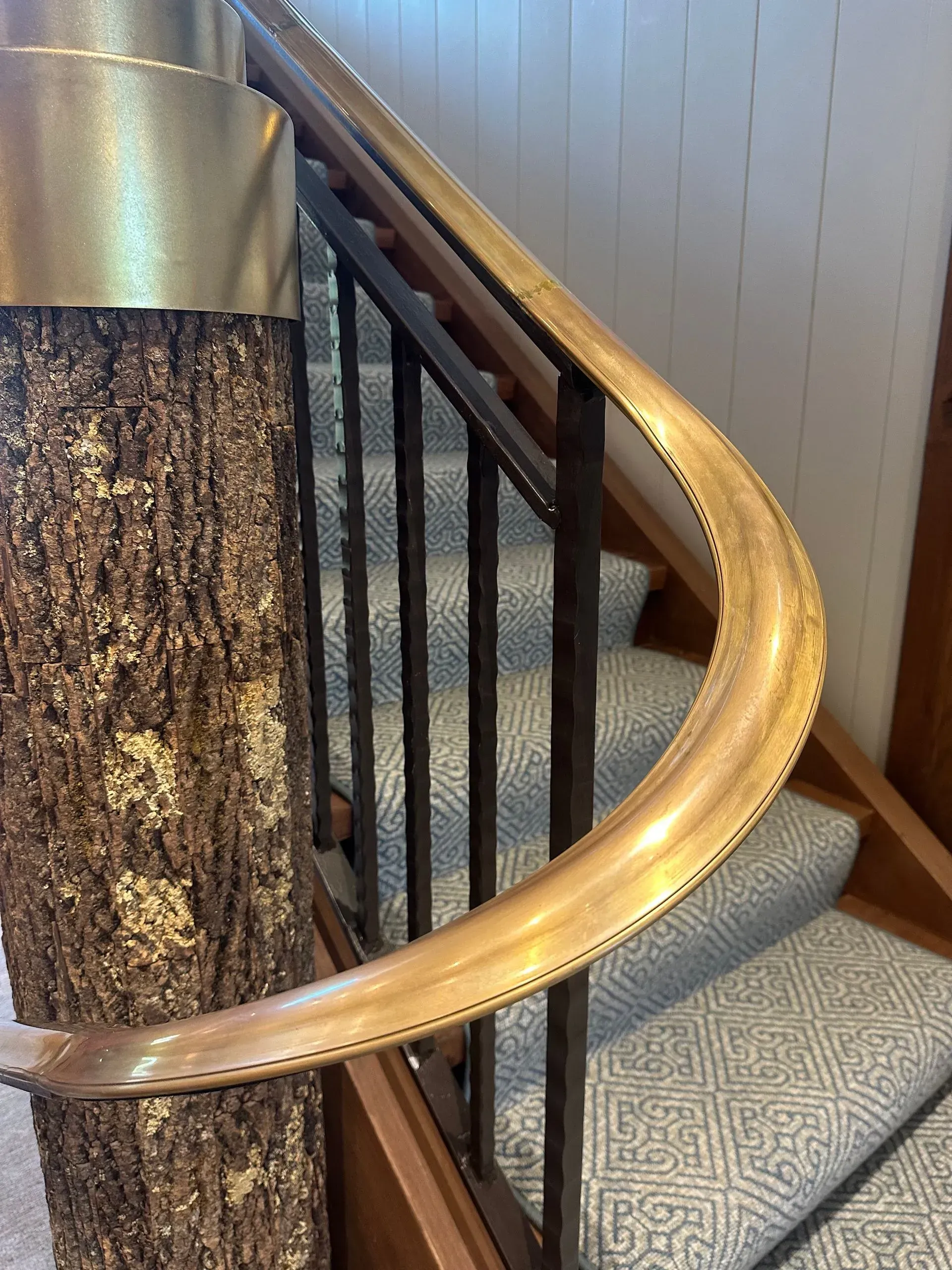 Staircase with wooden handrail, metal railing, and carpeted steps. Tree trunk pillar is visible on the left.