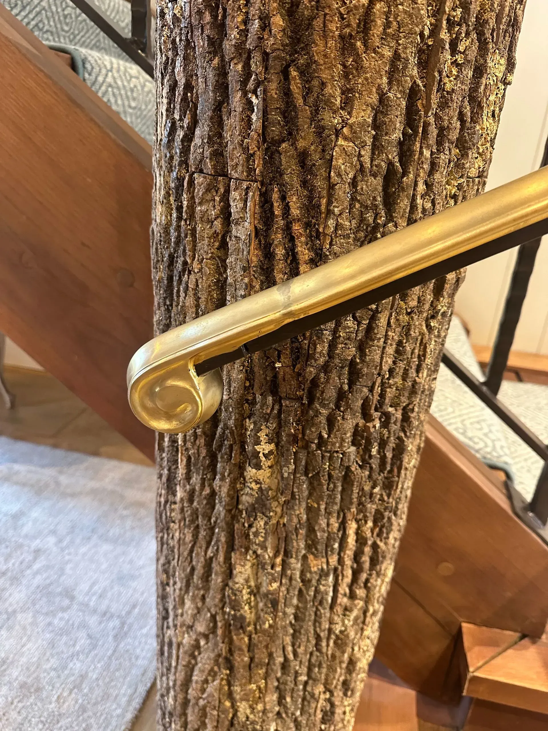 A gold handrail attached to a tree trunk post supports stairs with carpet.