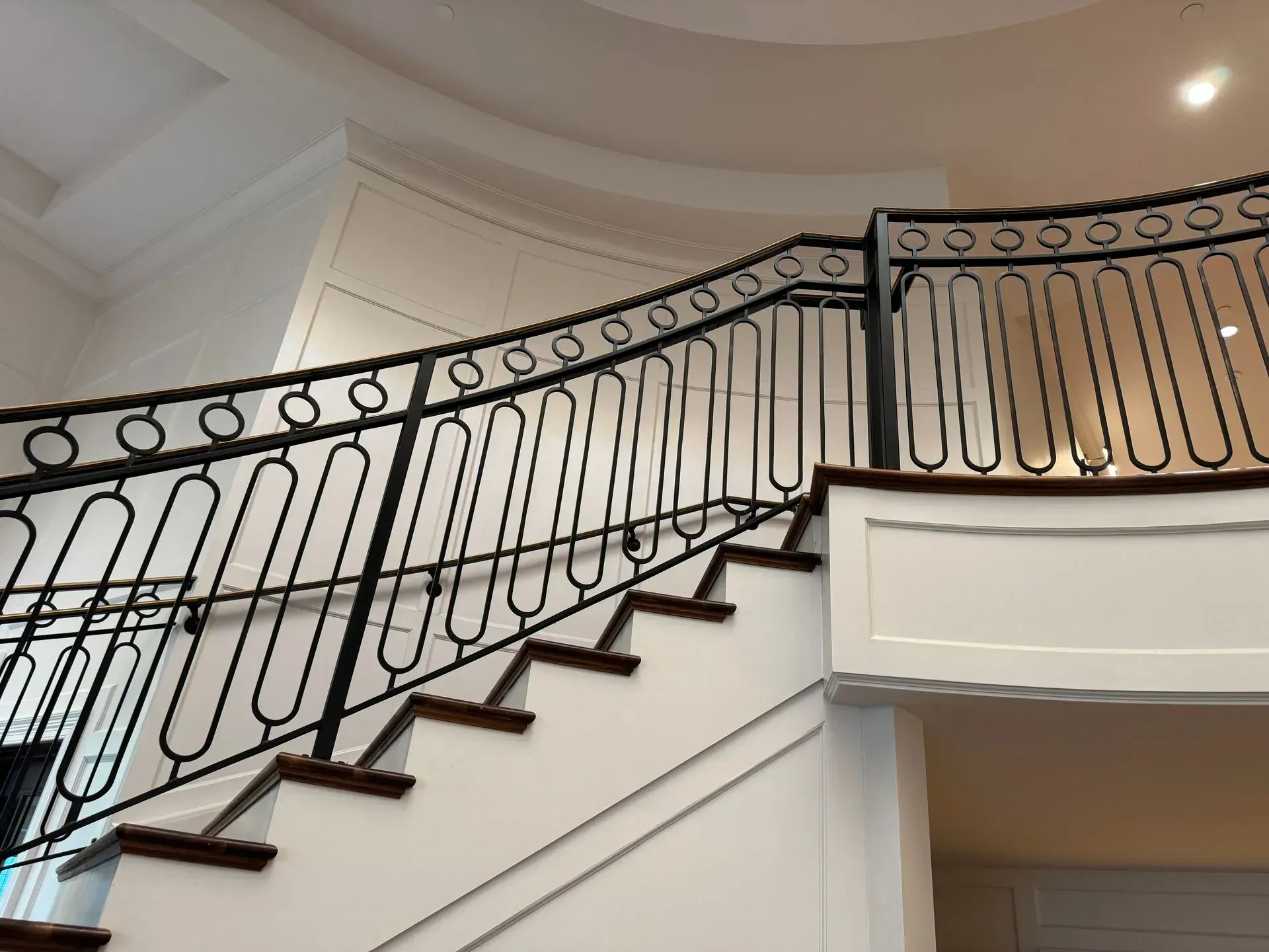 Black metal railing on a curved staircase with white walls and wood steps.