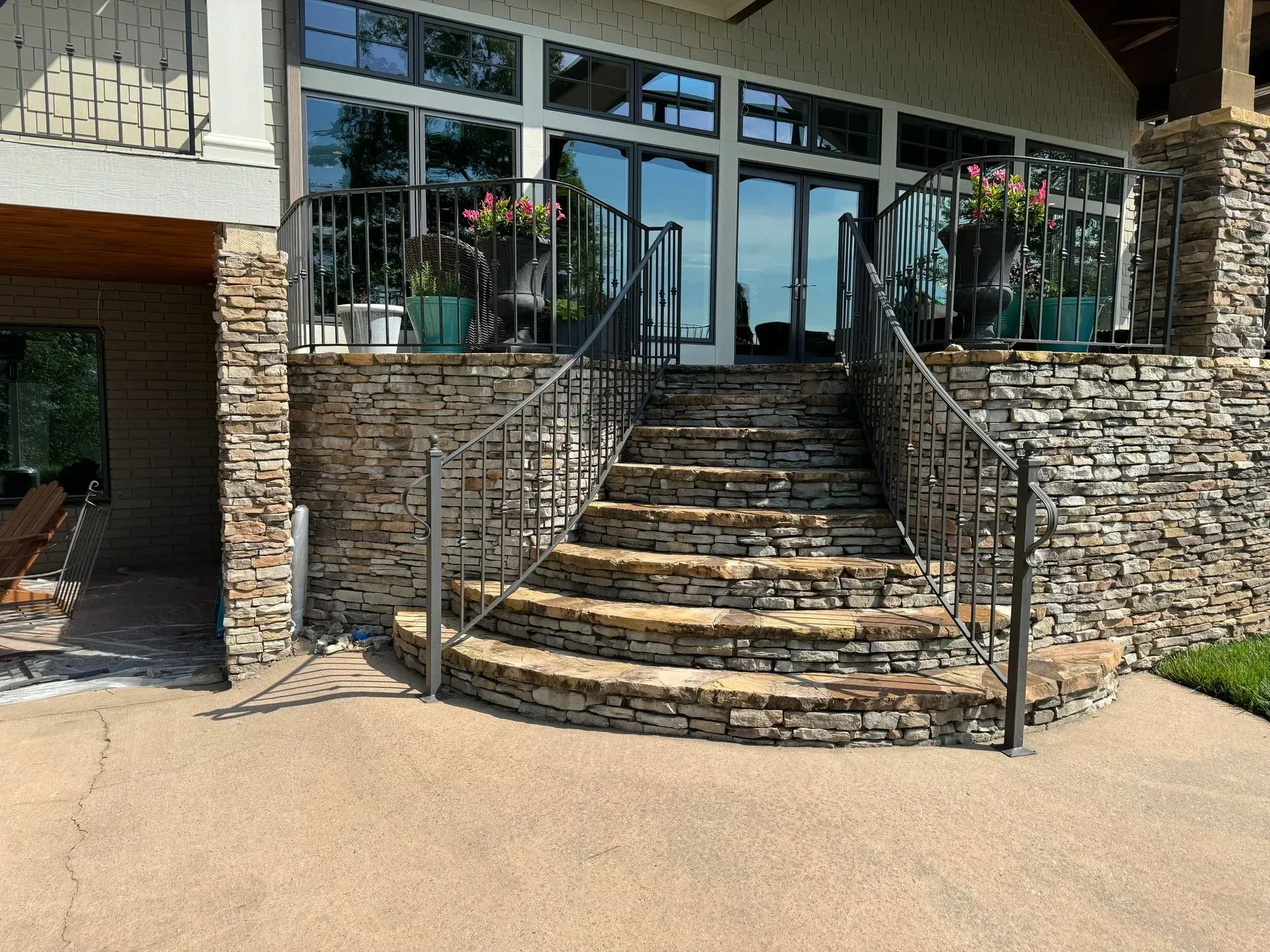 Stone steps with black railing leading up to a house with glass doors and windows, potted plants.