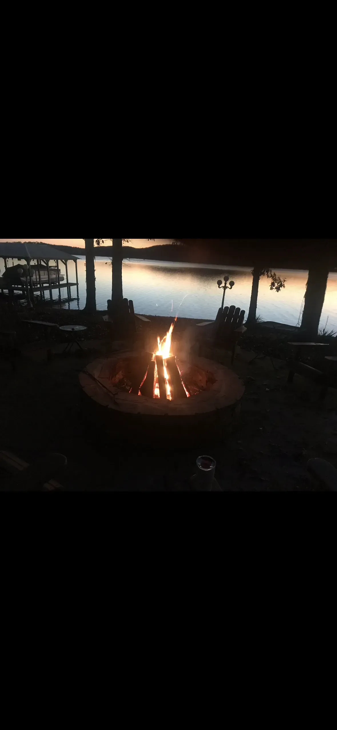 A fire pit on a patio by a lake at dusk.