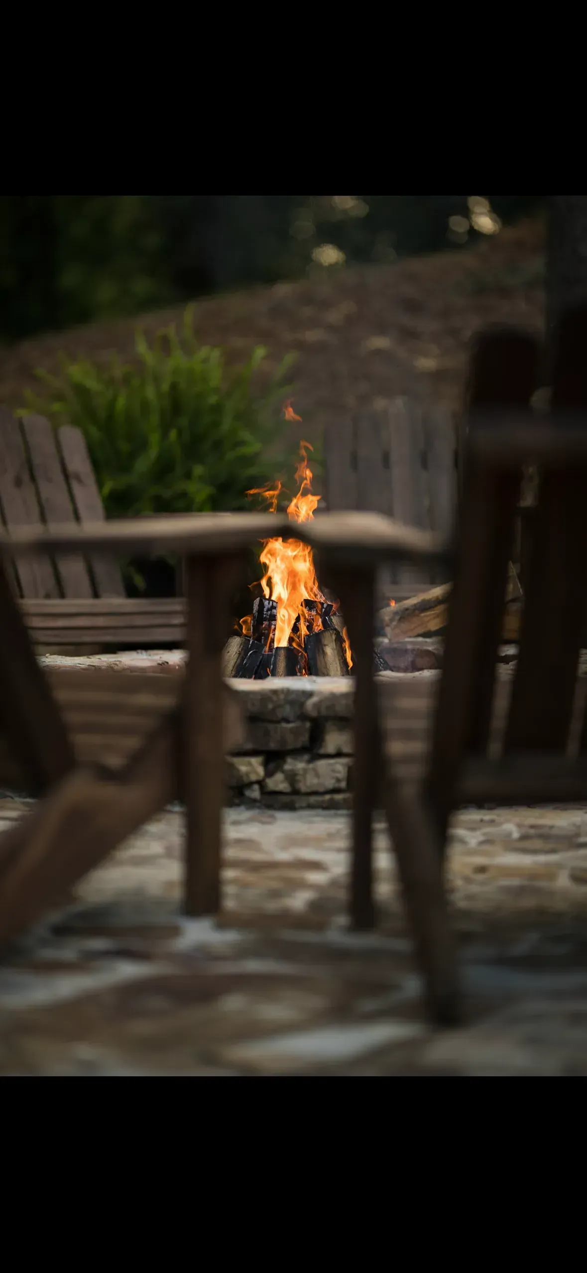 Fire pit between wooden chairs, with flames burning brightly.