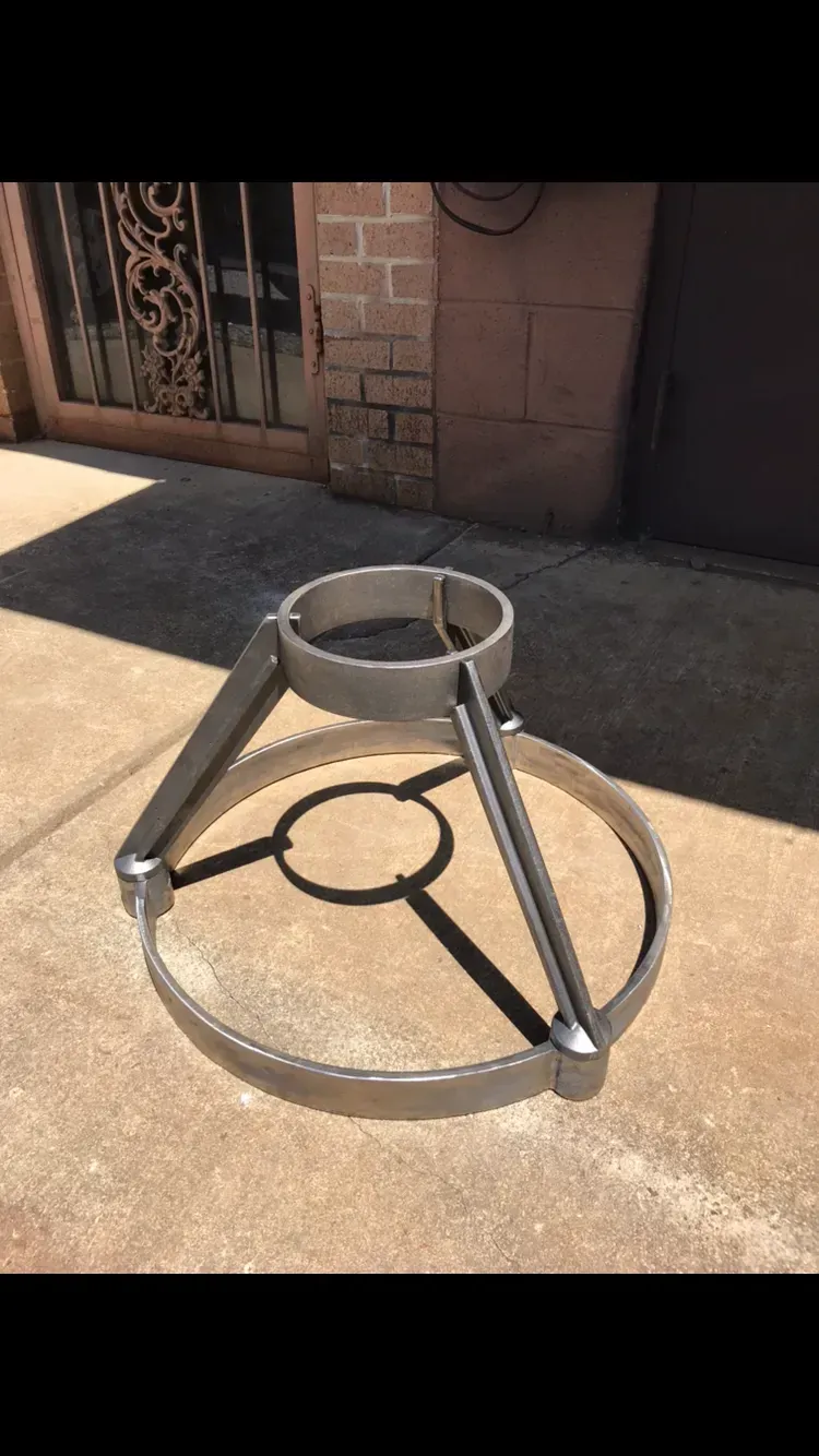 Metal tripod stand on concrete, with circular base and top ring, outdoors.