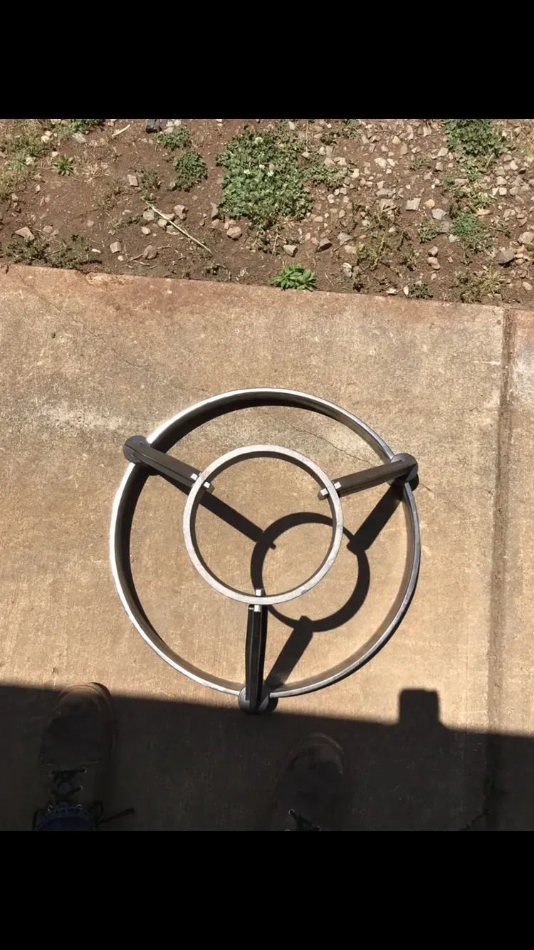 Metal table frame with three-legged base on concrete patio, casting shadows in sunlight.