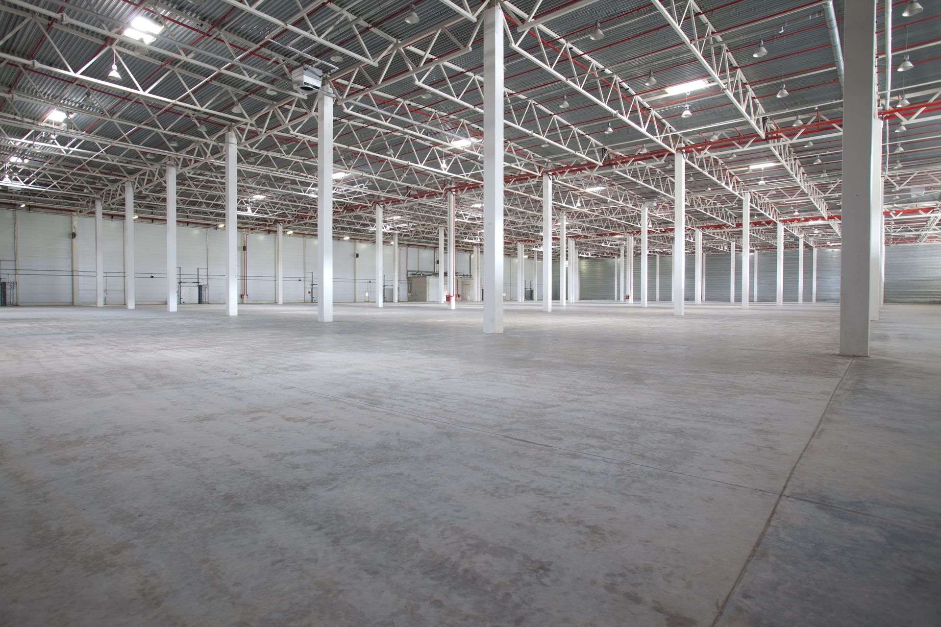 Large, empty warehouse interior with concrete floor, white support columns, and metal roof structure.