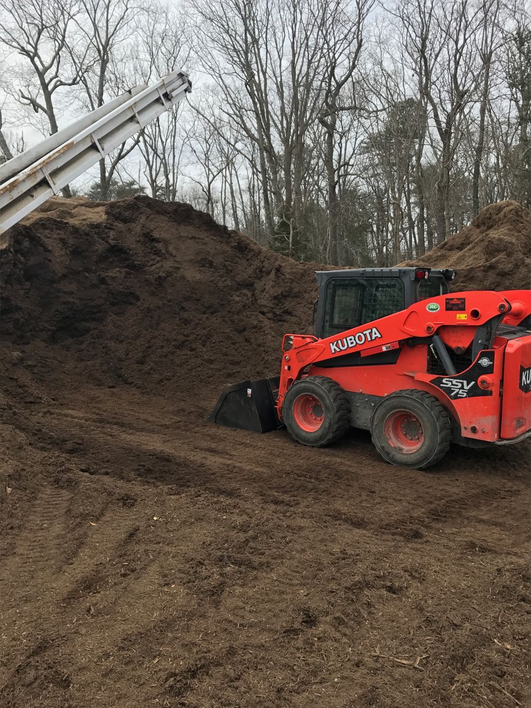 A red skid steer is loading dirt into a pile.