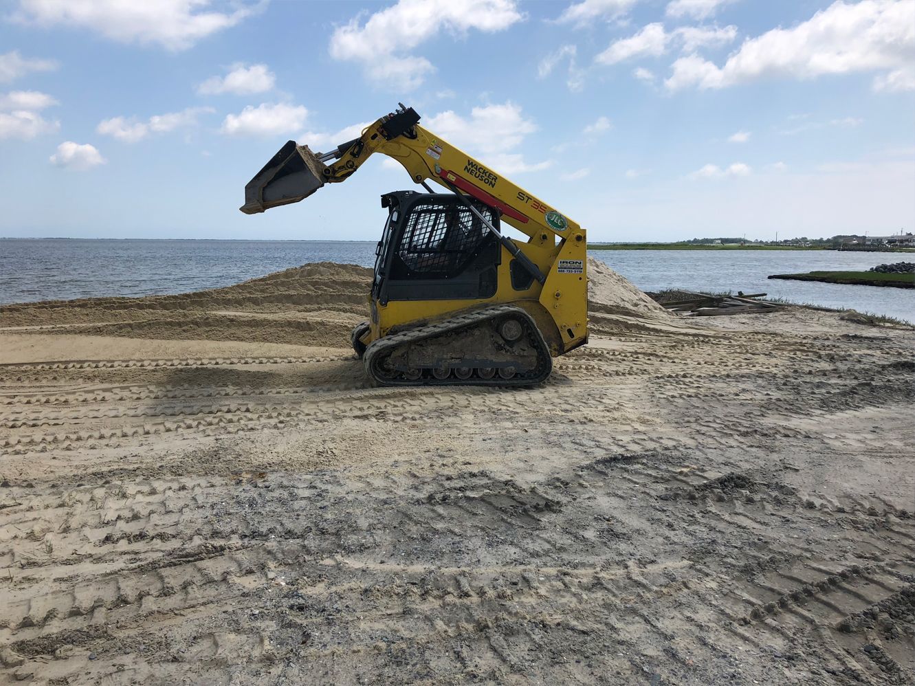 A yellow bulldozer is driving on a dirt road next to a body of water.